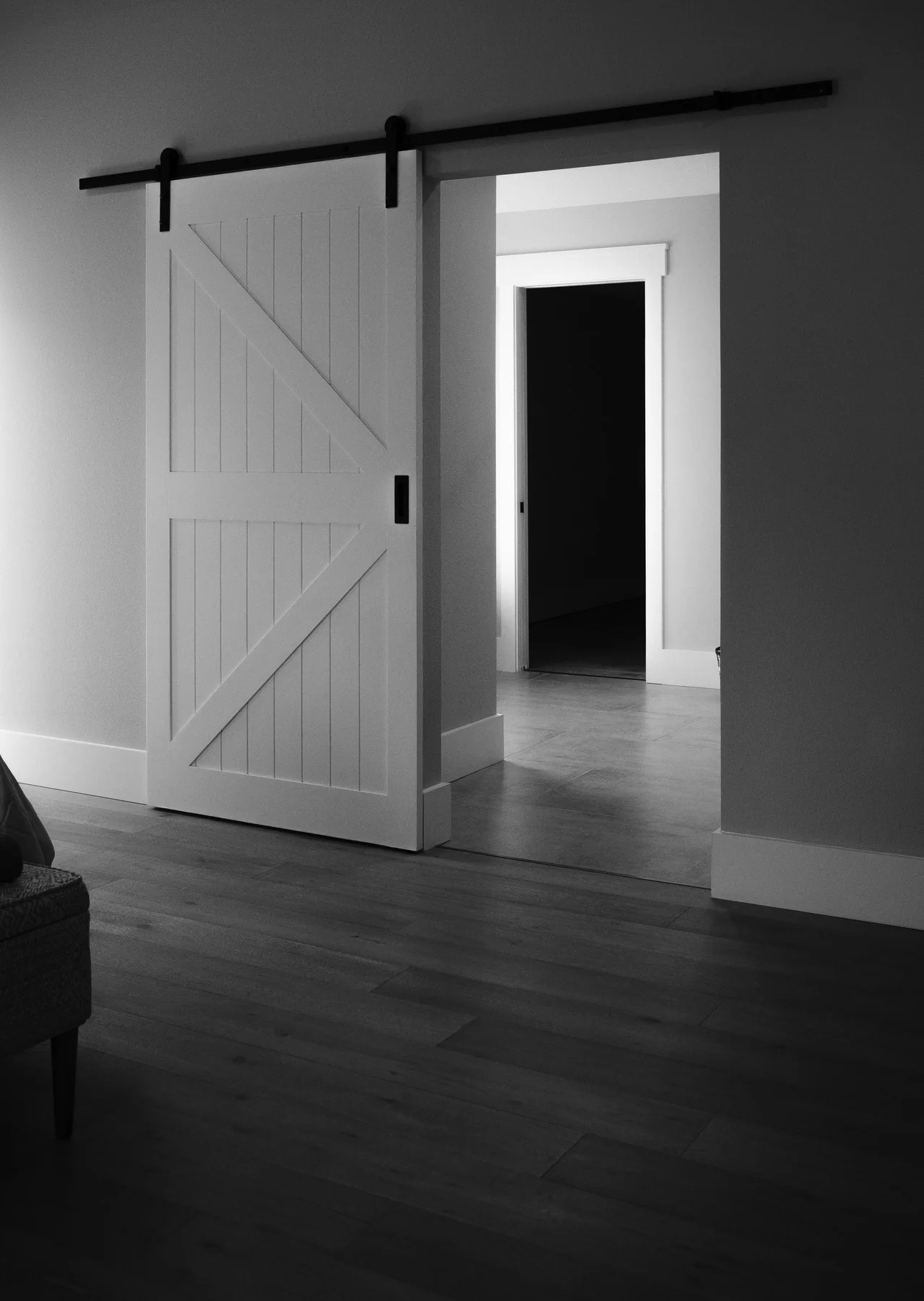 Black-and-white interior view through an open barn door into a shadowed hallway.
