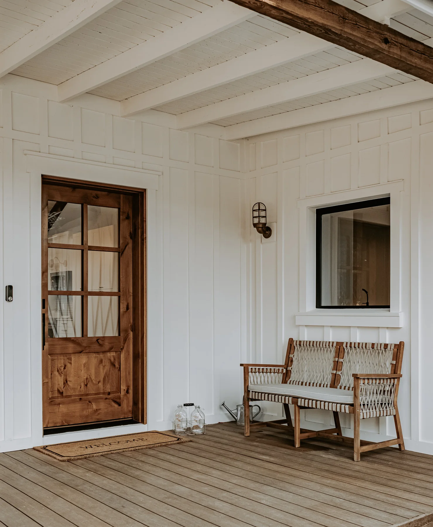White exterior porch with woven chairs, a wood door, and a black-framed window.