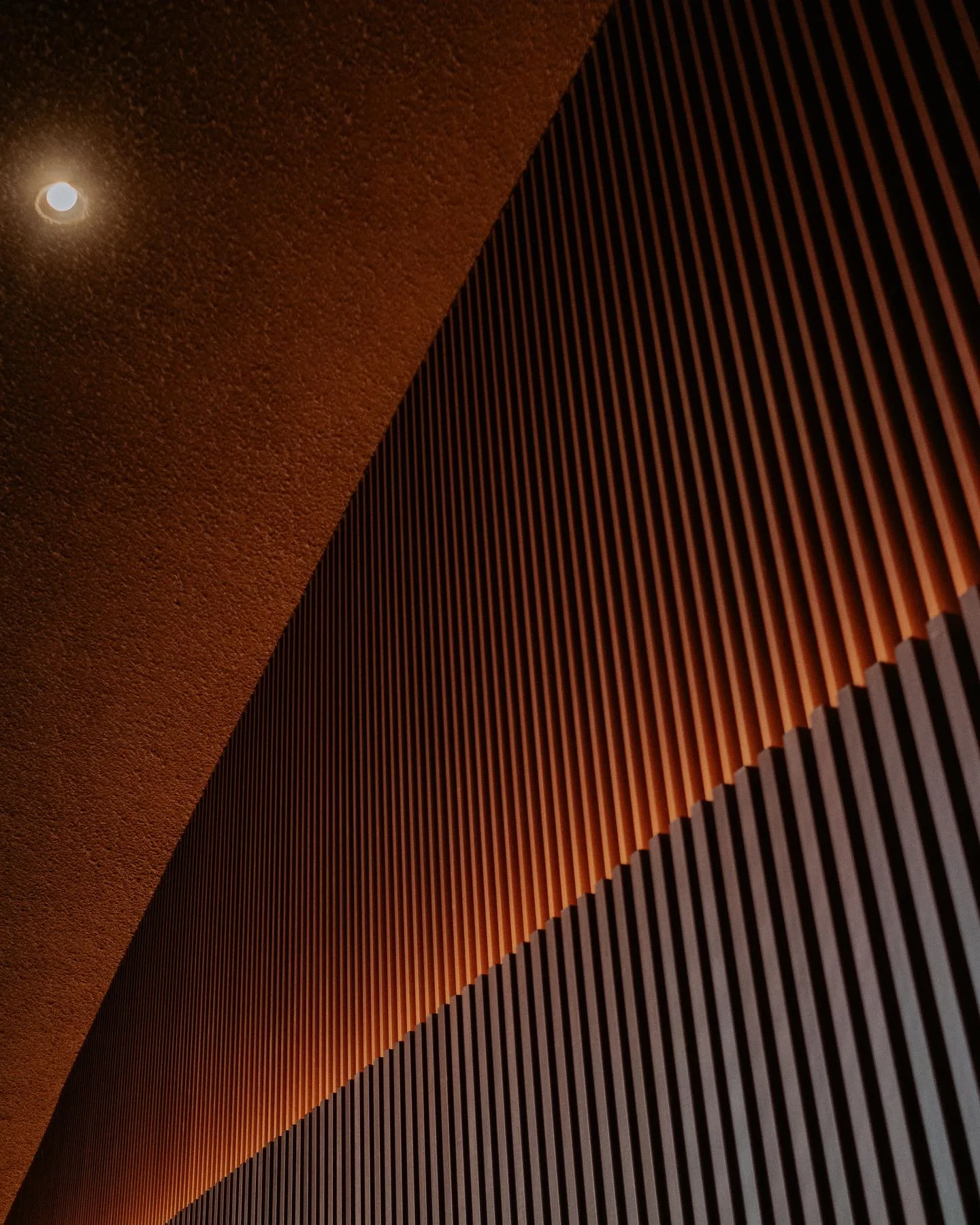 Warm geometric view looking upward through a slatted wood stairwell.