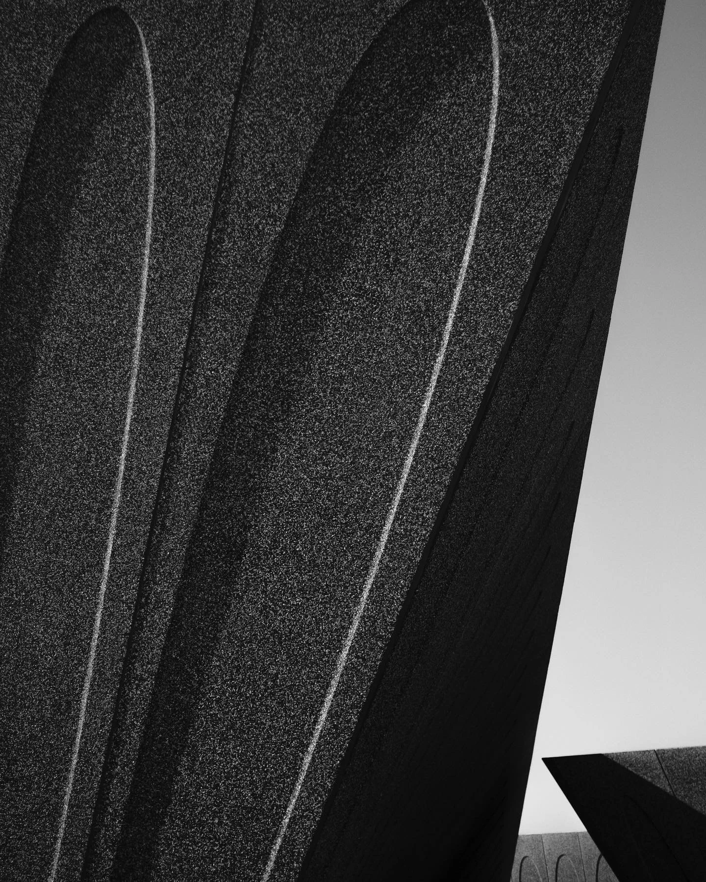 Dark vertical ridged architectural surface in high contrast against a white wall.