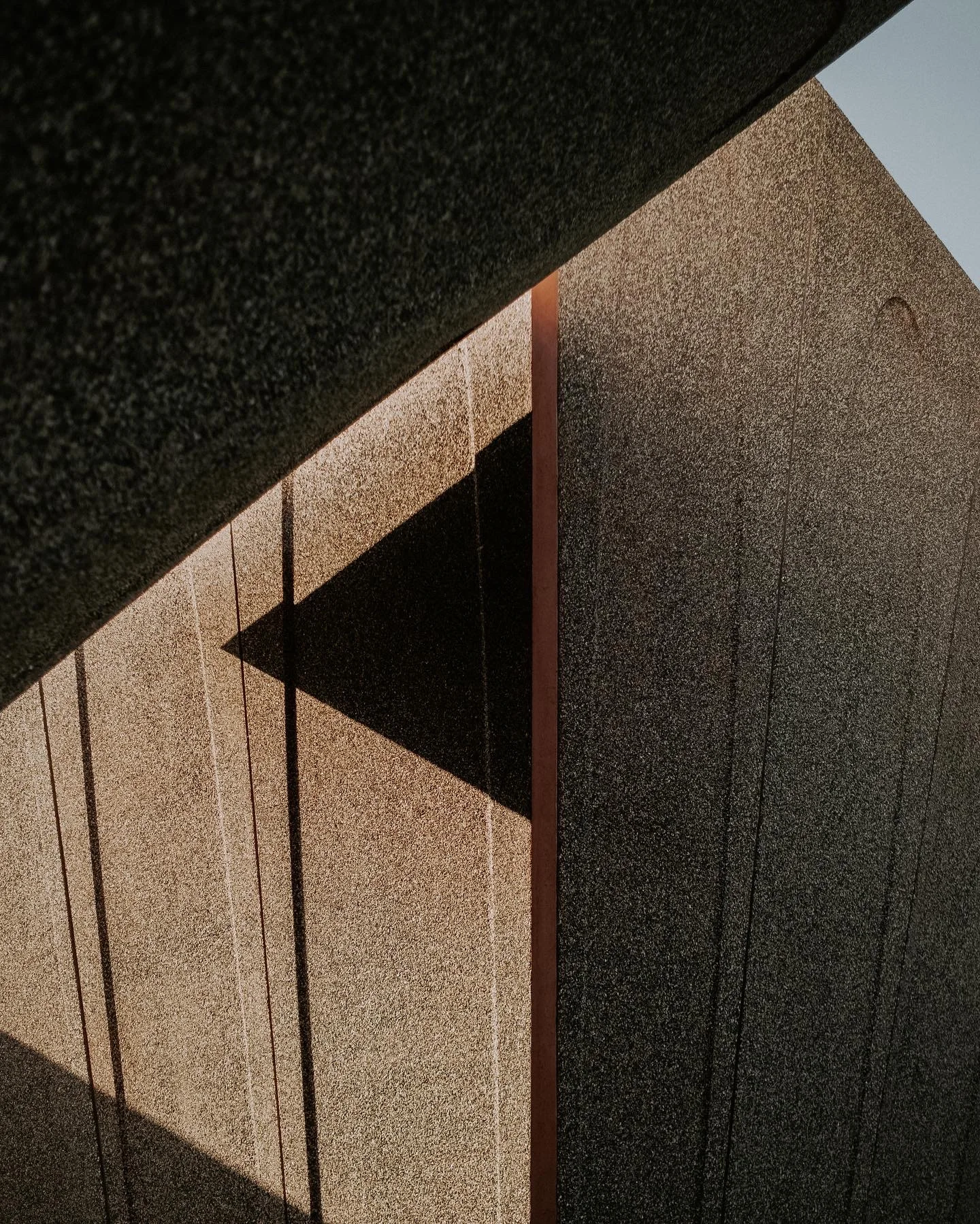 Geometric shadow cast across a textured warm-gray architectural panel.