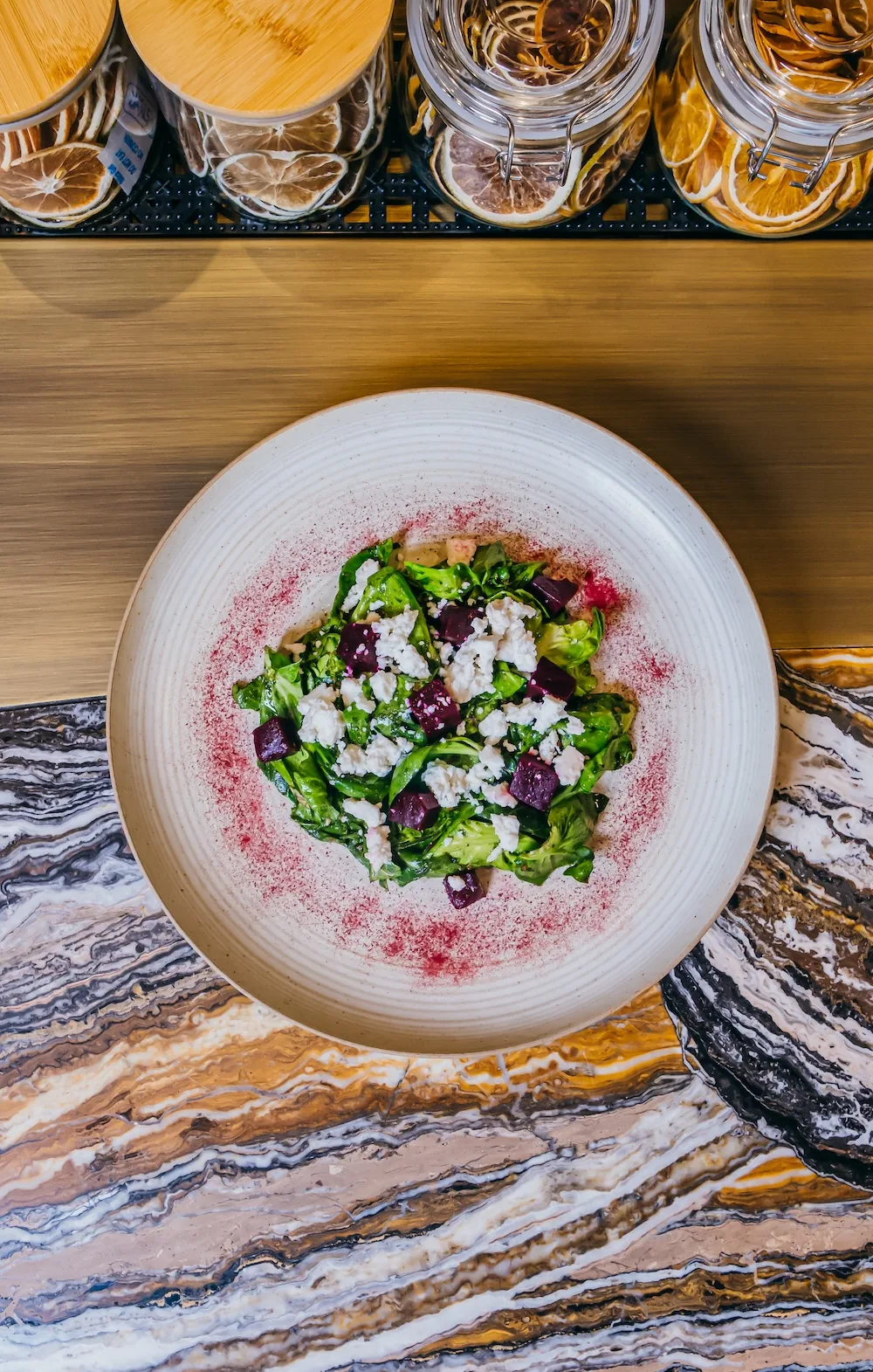 Beet salad with greens and crumbled cheese on a white ceramic plate.