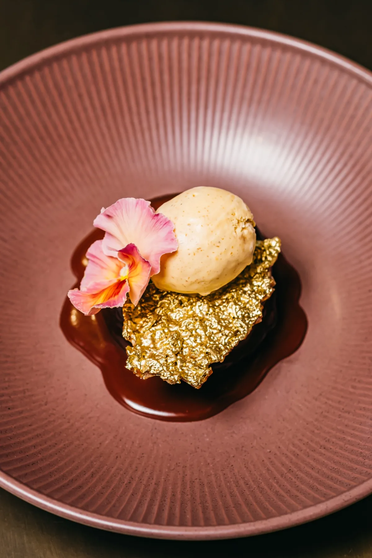 Golden dessert in a pink bowl, finished with a hibiscus flower.