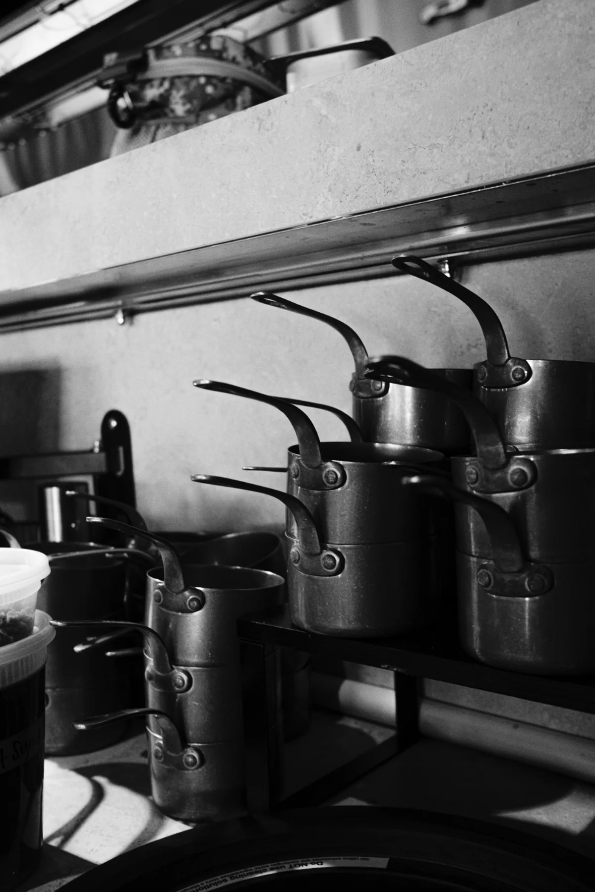 Commercial kitchen line with black stockpots beneath a metal shelf.