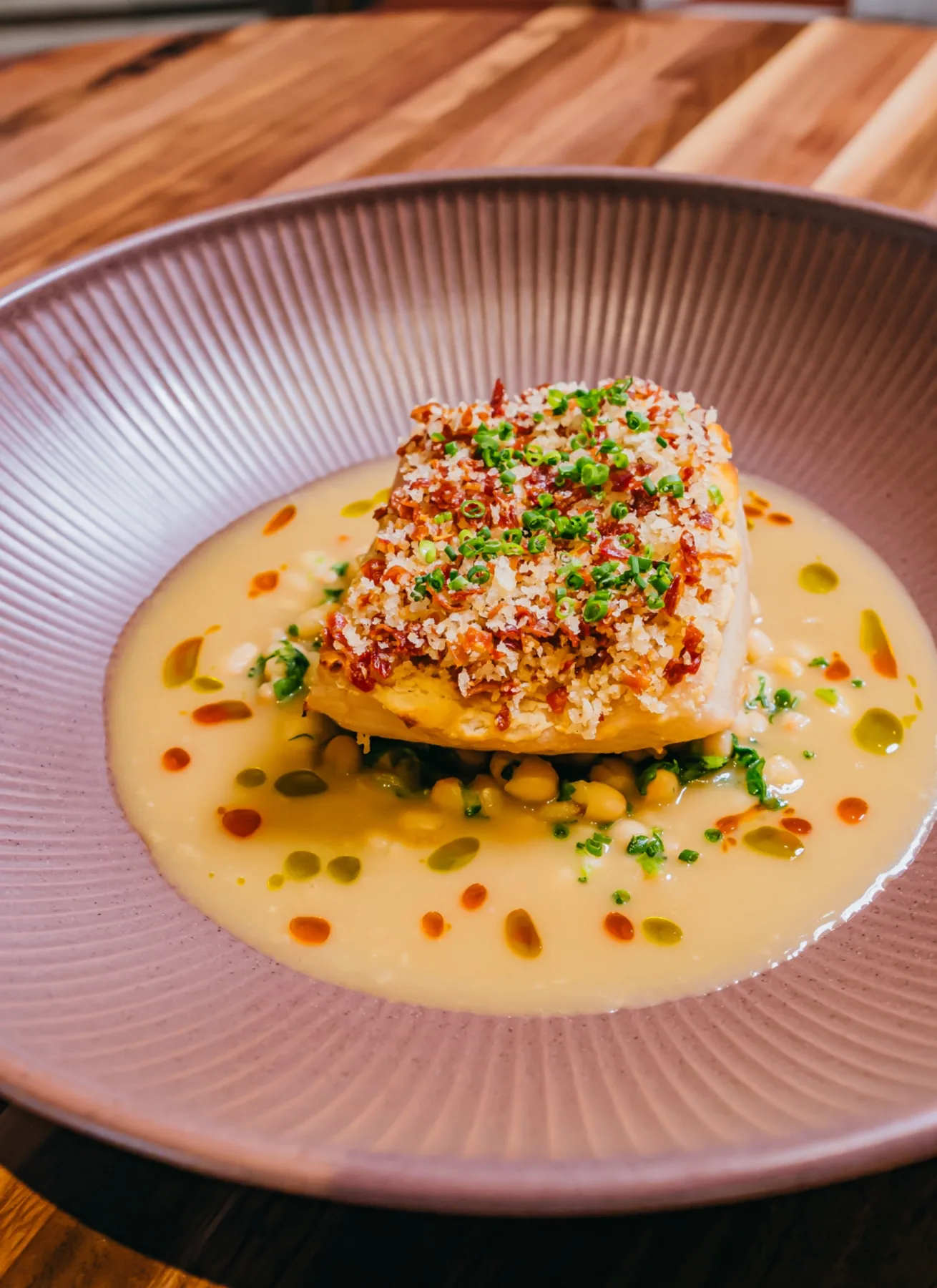 Crisp-skinned sea bass plated over vegetables in a pale sauce.