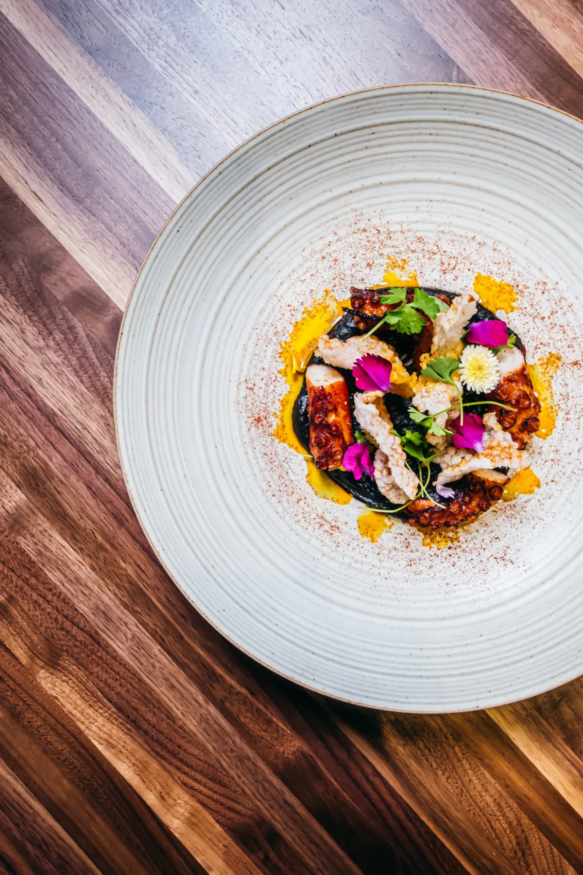 Grilled octopus plated with greens and edible flowers.