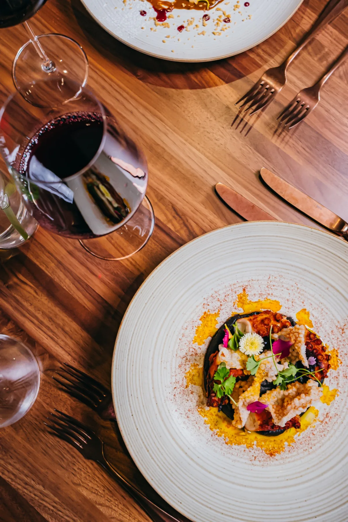 Top-down composed dish beside a glass of red wine on a wood table.