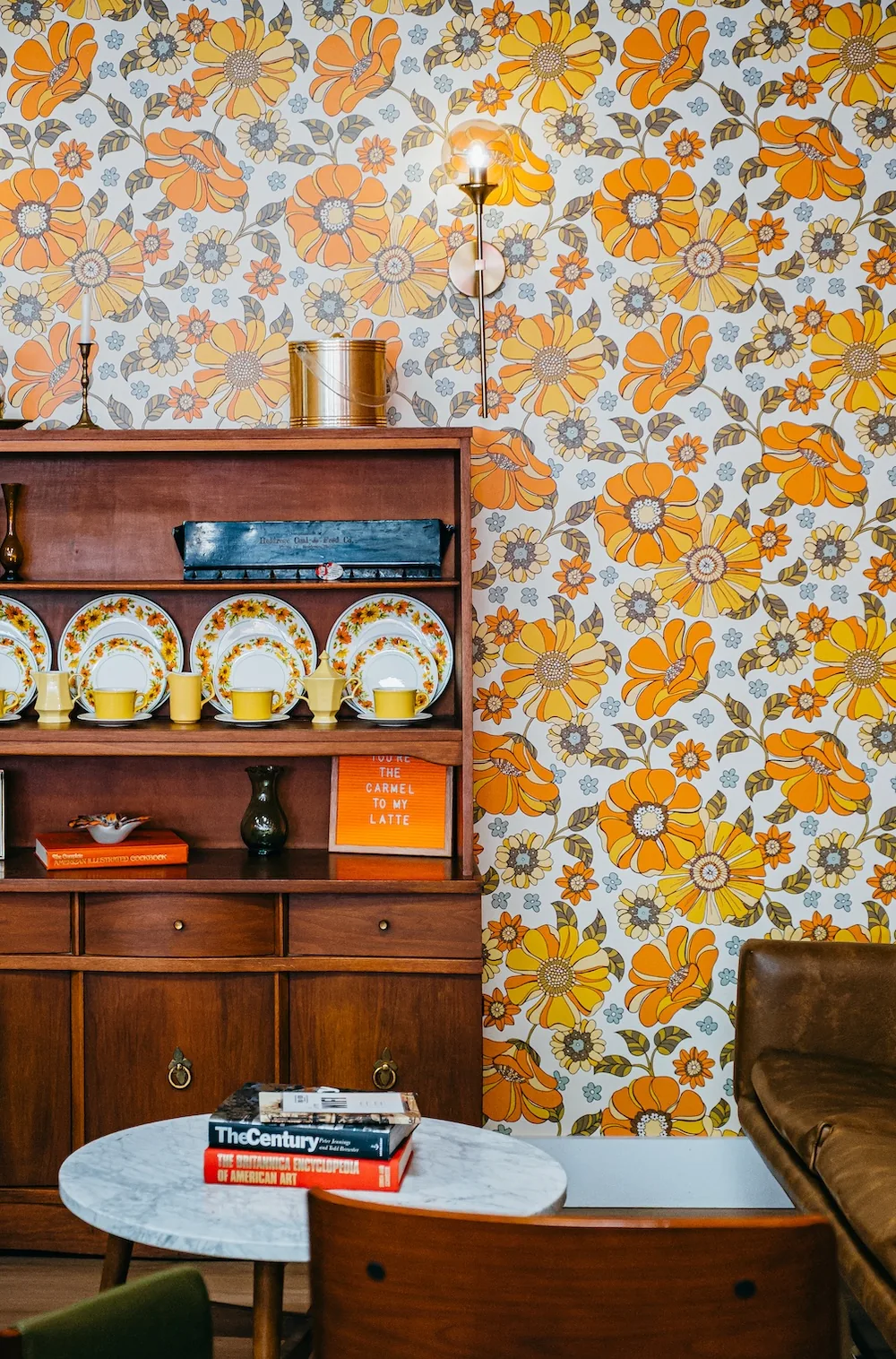 Vintage wood shelf with floral wallpaper, yellow mugs, and patterned ceramic plates.