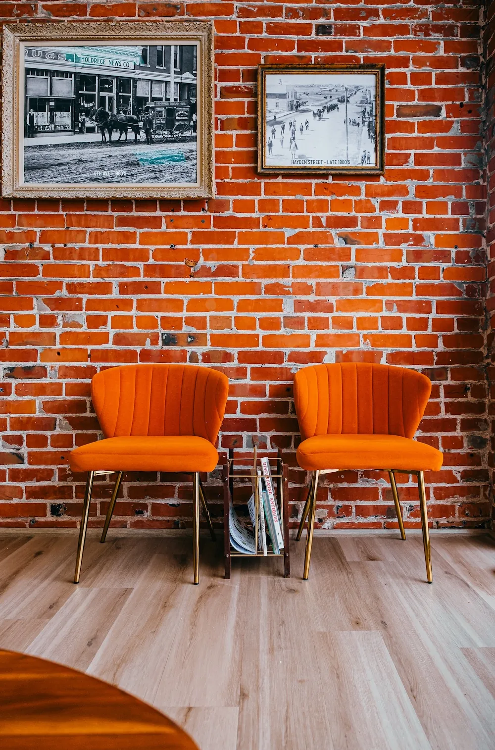 Orange velvet chairs against exposed brick and floral wallpaper.