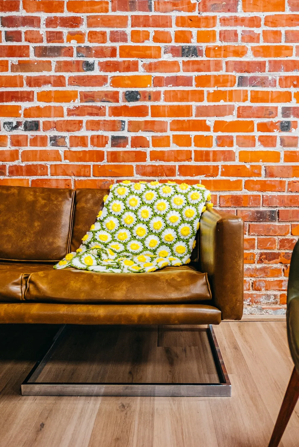 Leather cafe bench with a flowered cushion against a red brick wall.