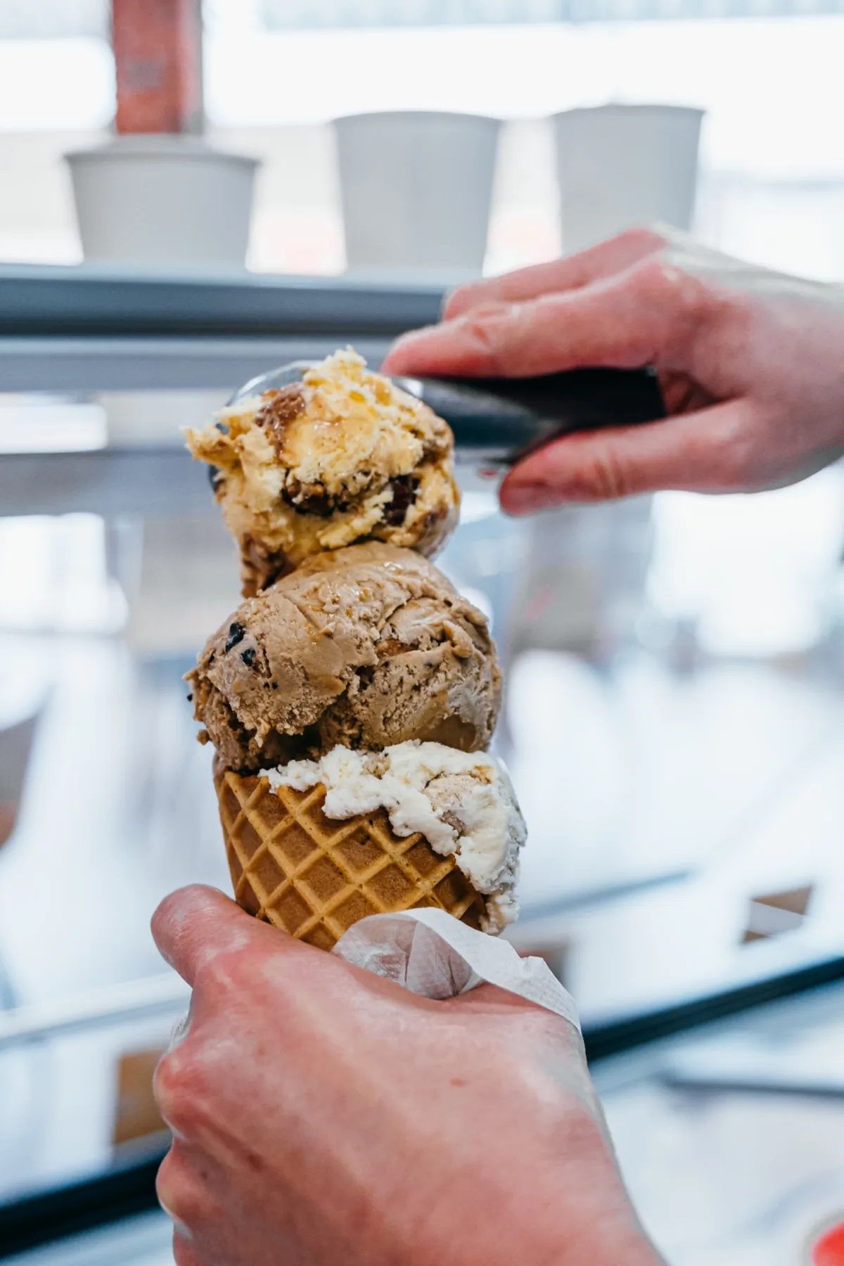 Hand holding a tall waffle cone stacked with scoops of ice cream.