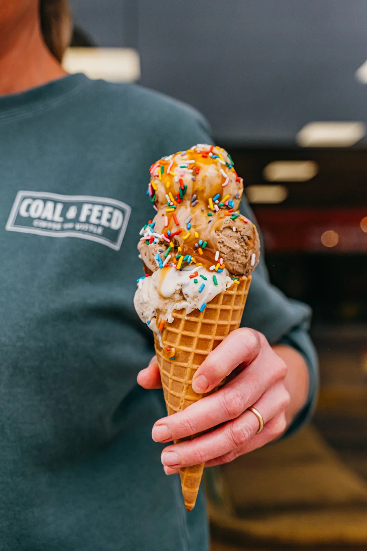 Sprinkle-topped ice cream cone held in front of a Coal and Feed logo sign.