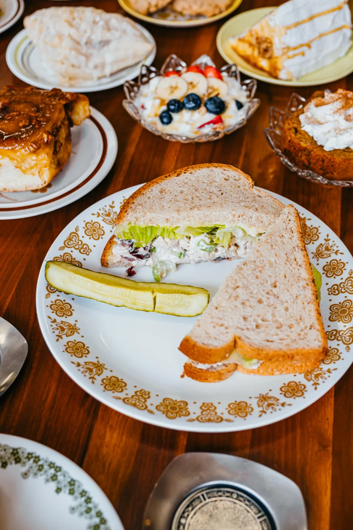 Creamy chicken salad sandwich with a pickle on a patterned plate.
