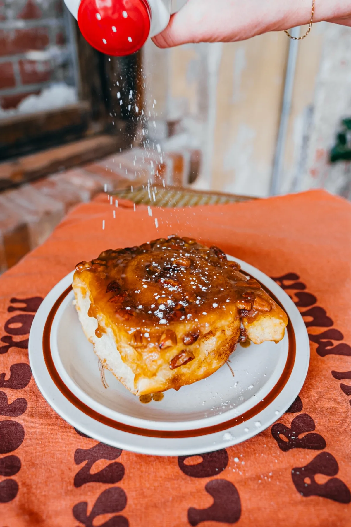 Warm cinnamon roll on a plate with glossy caramelized topping.