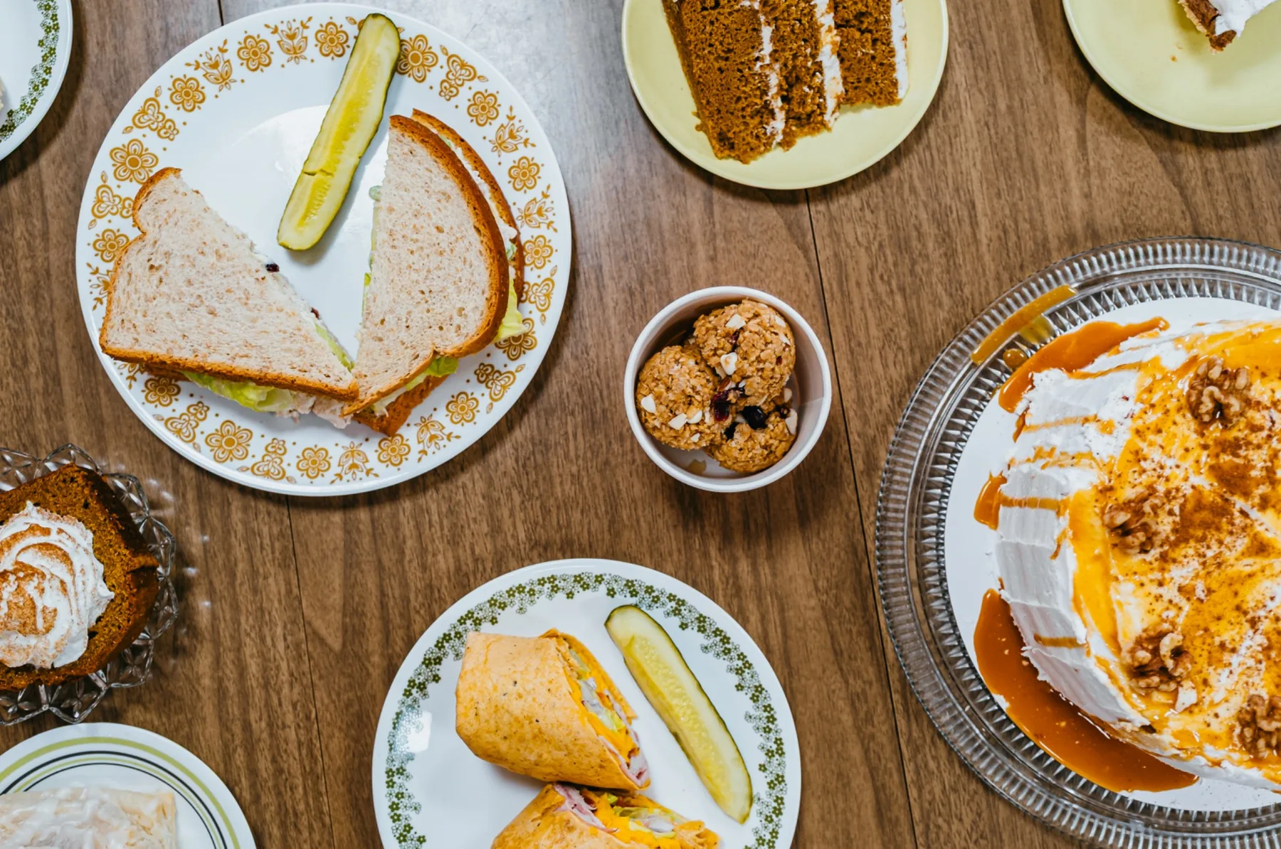 Overhead cafe table with patterned plates, pastries, and layer cake.
