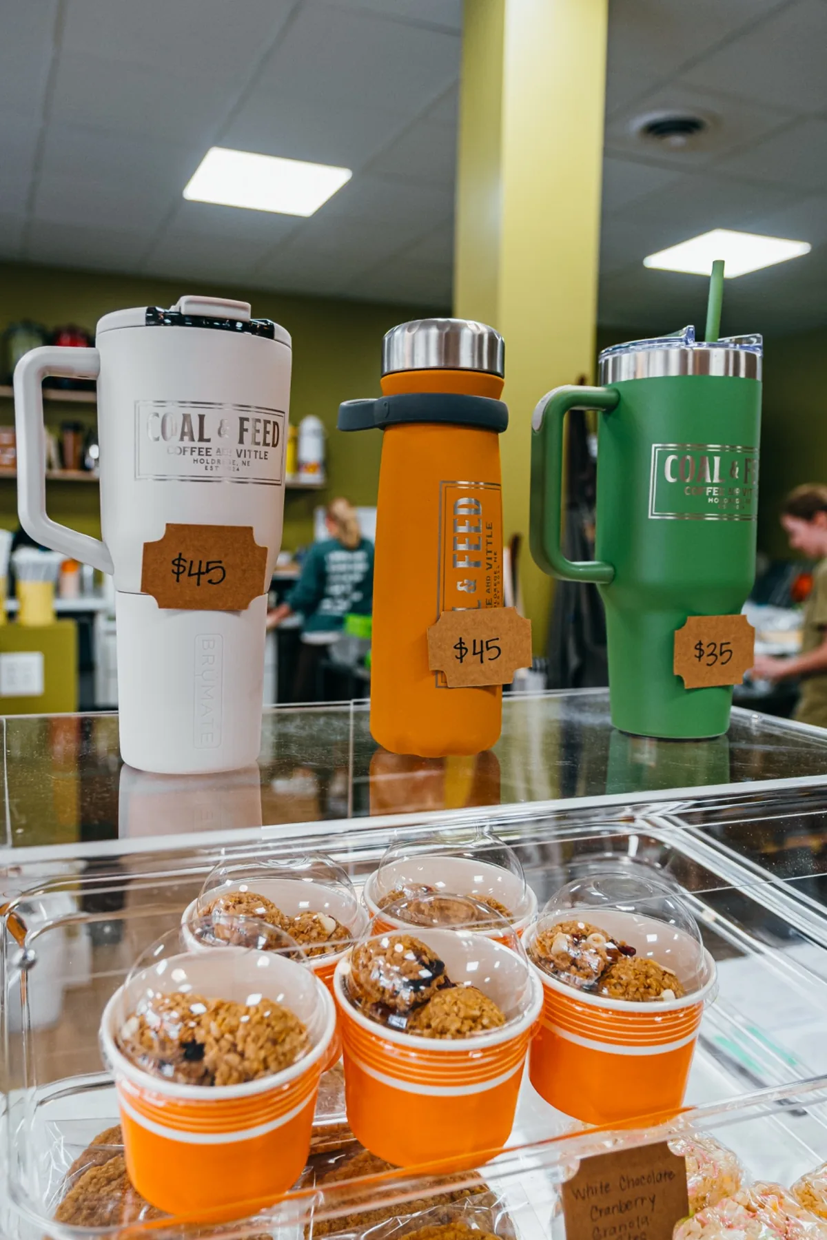 Coal and Feed branded travel mugs arranged on a glass counter.
