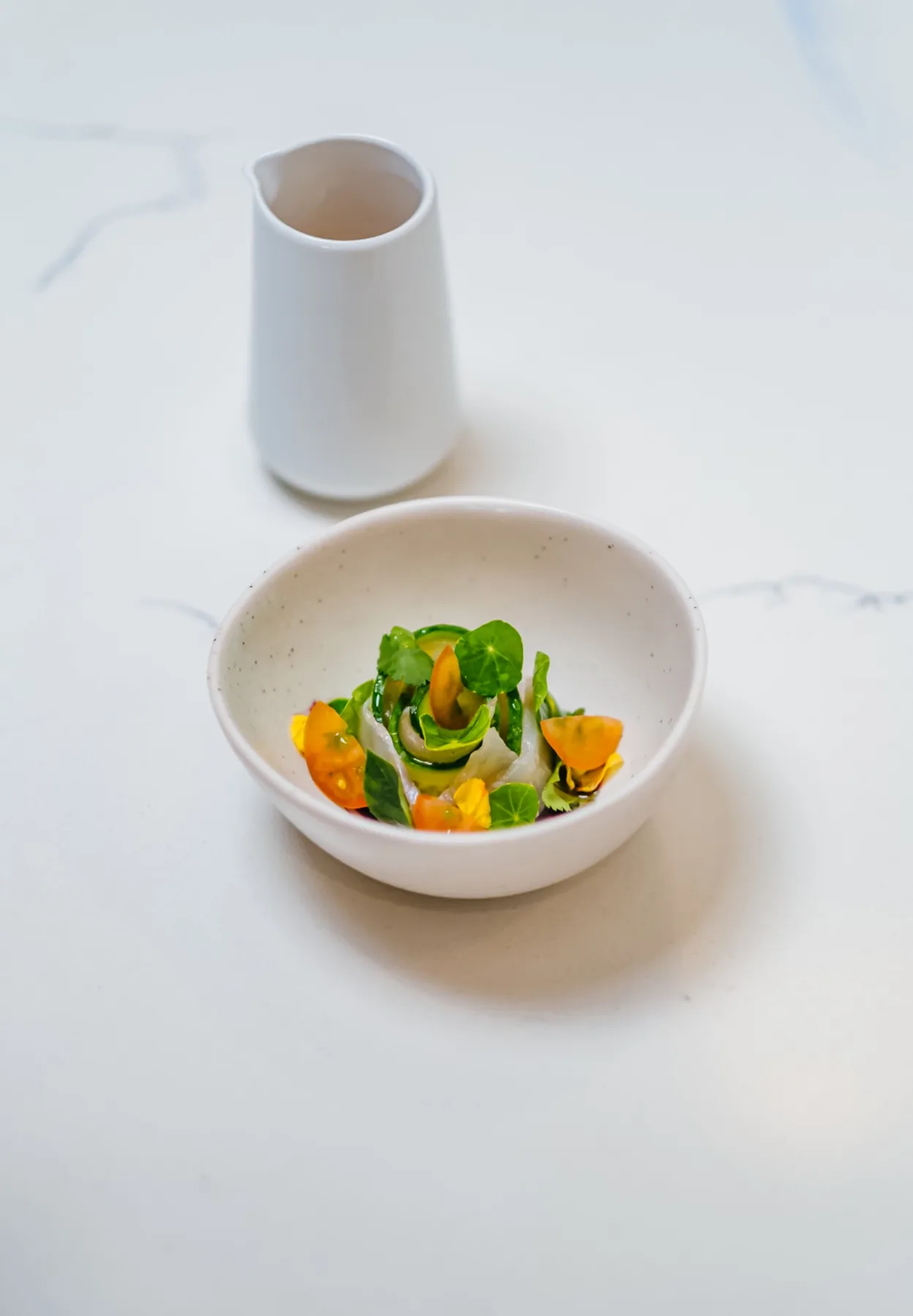 Small composed vegetable dish in a white bowl on a marble table.