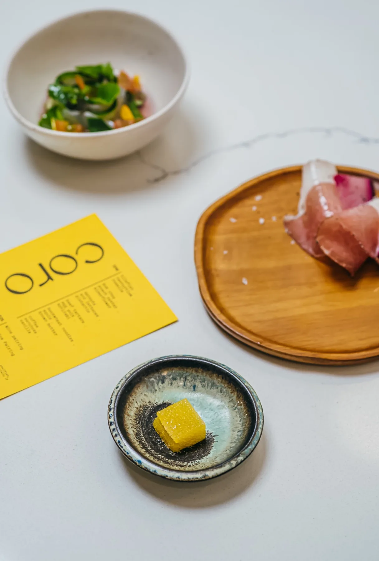 Yellow Coro menu and shared small plates arranged on a marble table.