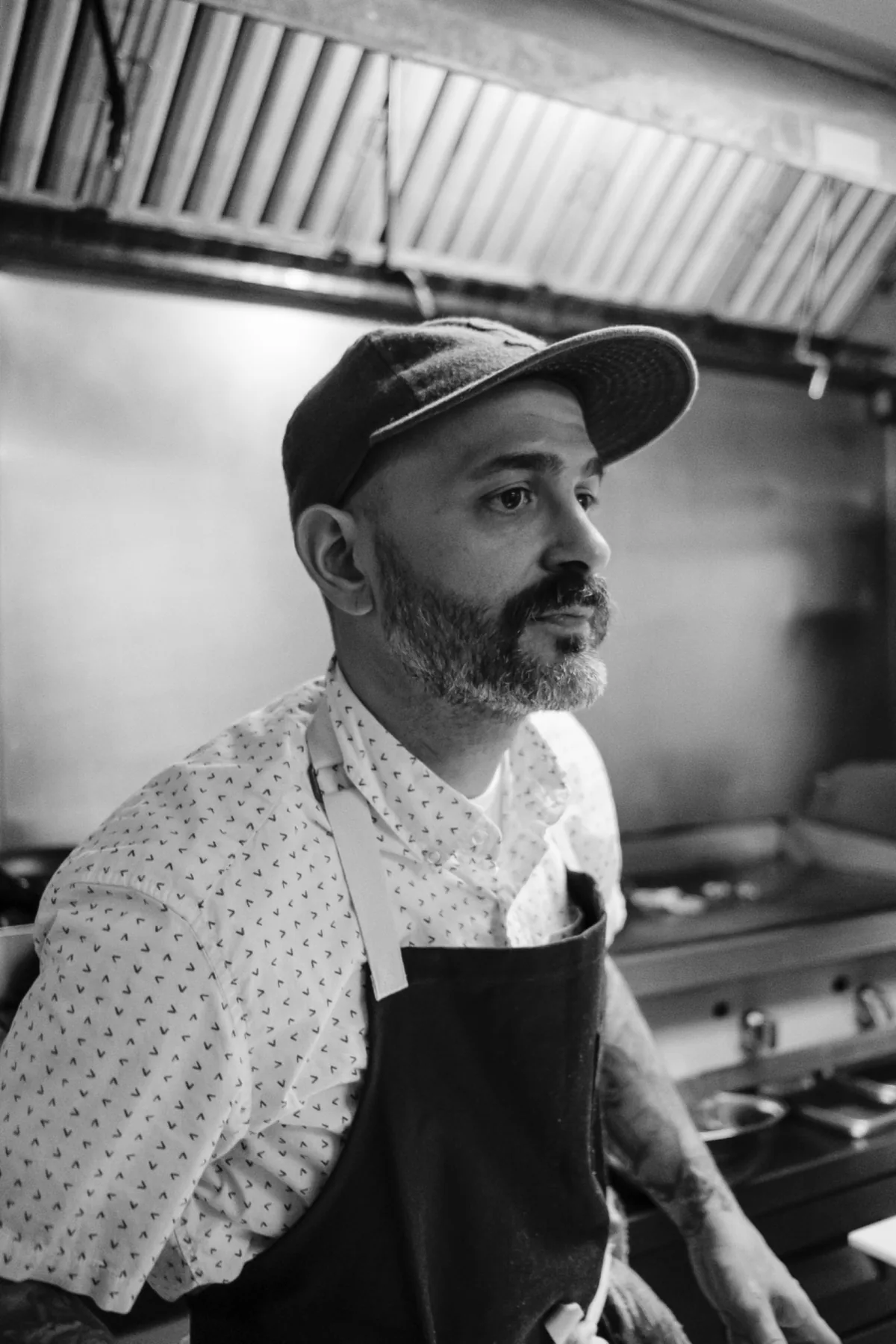 Black-and-white portrait of a bearded chef in a cap and apron.