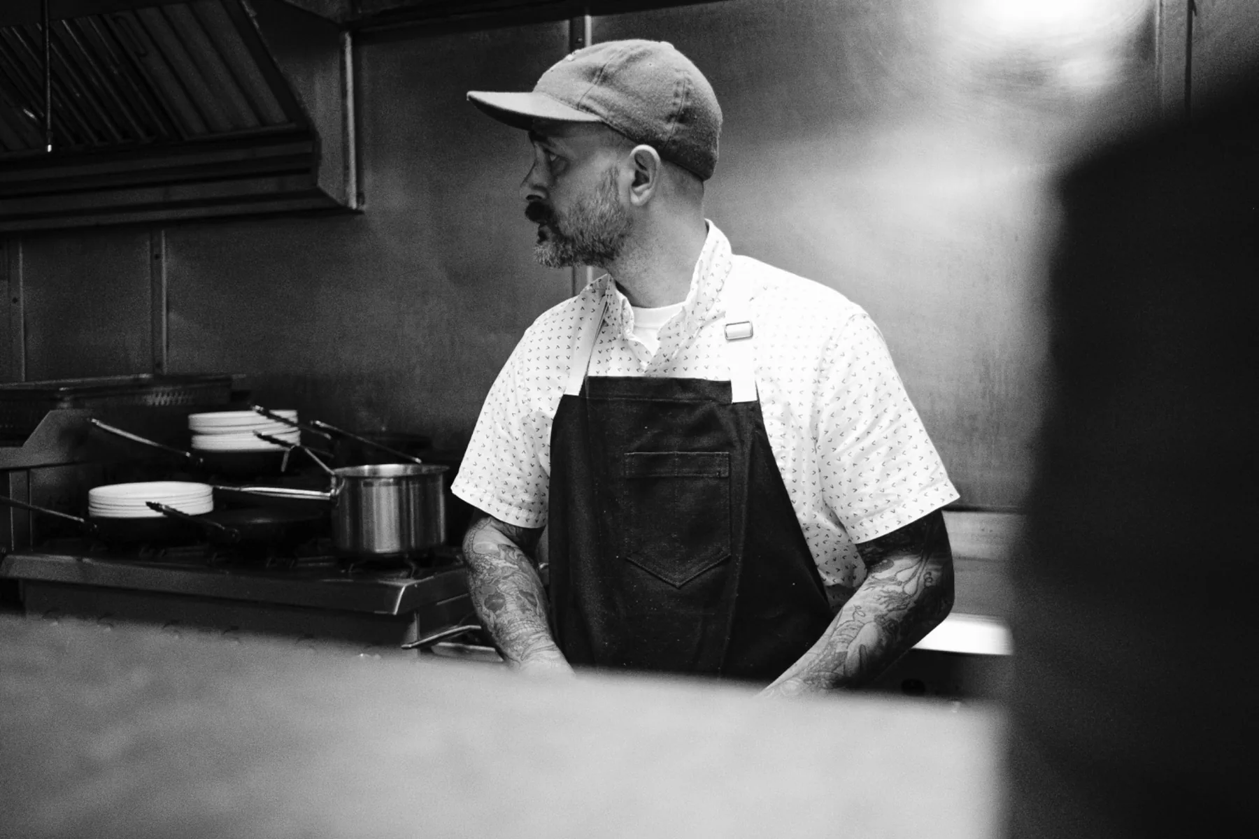 Black-and-white chef portrait beside a busy restaurant stove.