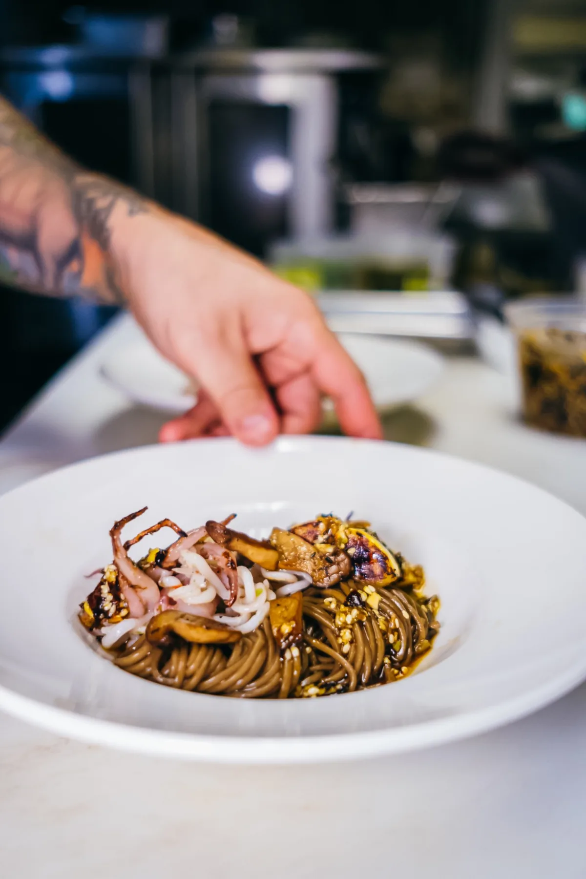 Chef places a finishing garnish on a bowl of noodles.
