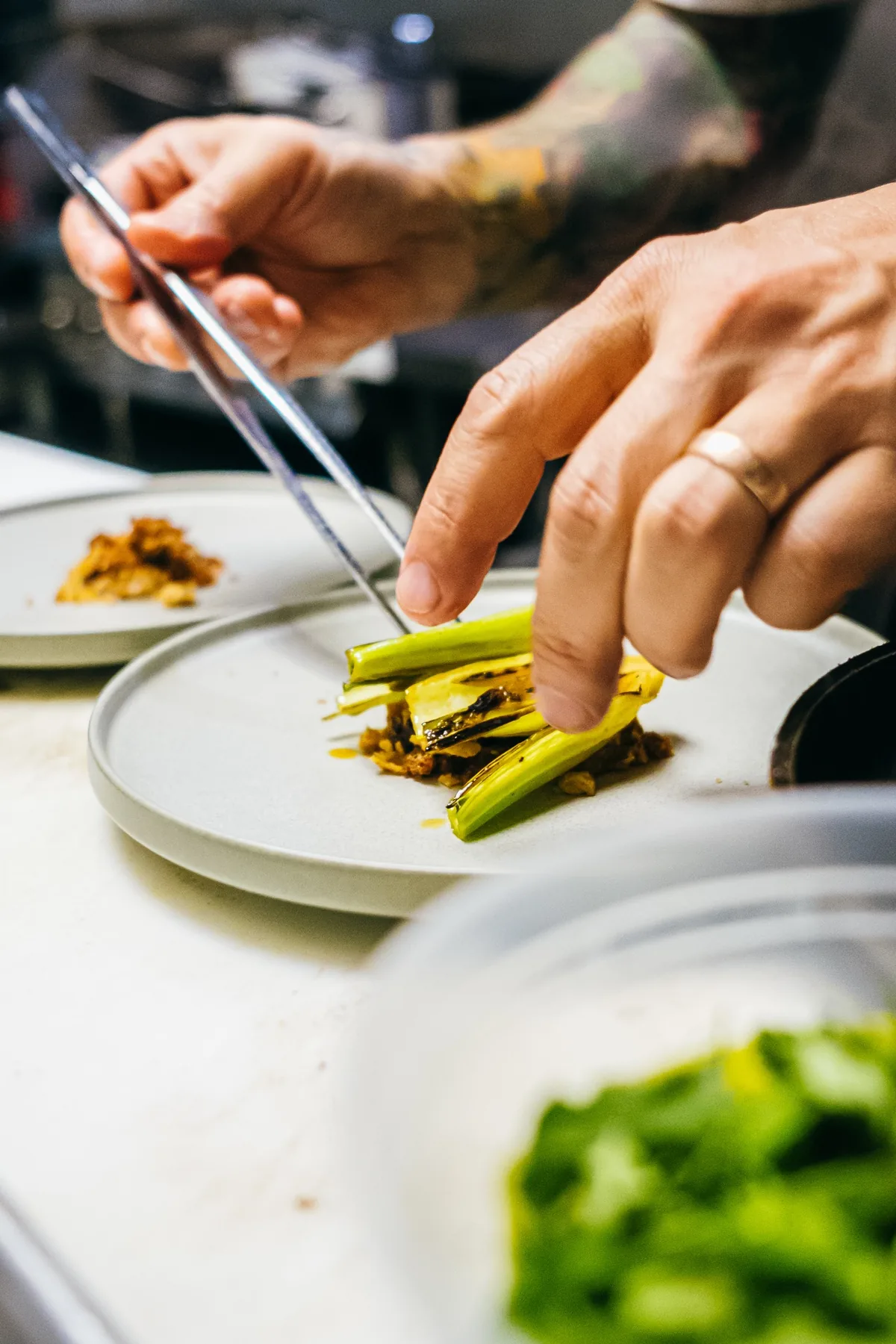 Chef uses tongs to plate grilled vegetables at the pass.