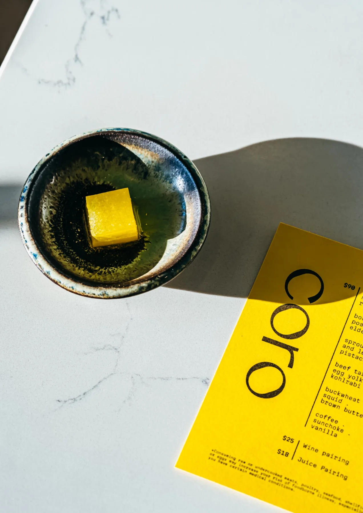 Golden square dessert in a black ceramic bowl beside a yellow menu.