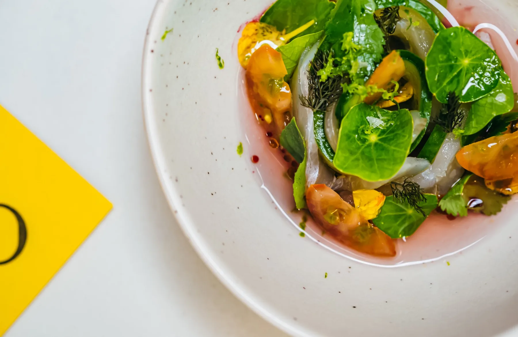 Close detail of a white bowl with greens and citrus on a marble table.