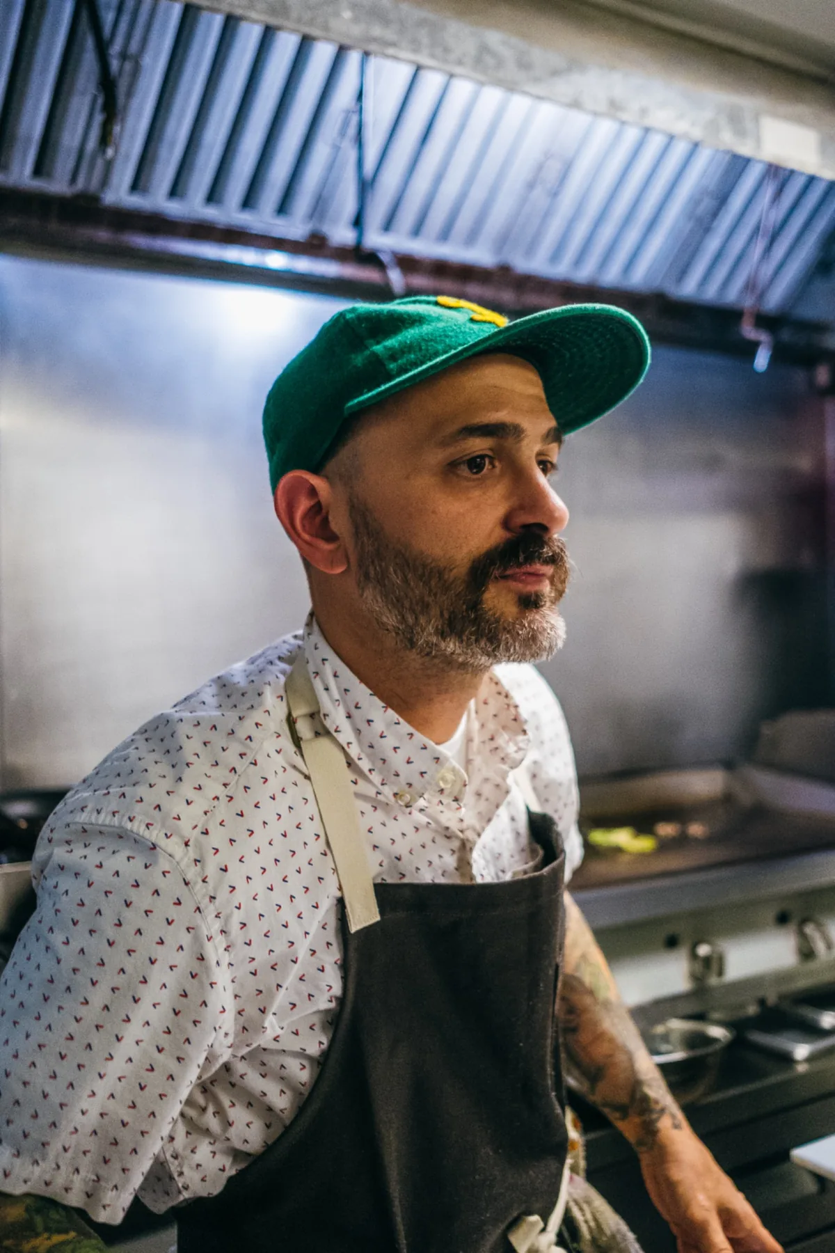 Profile portrait of a chef in a green cap at the stove.