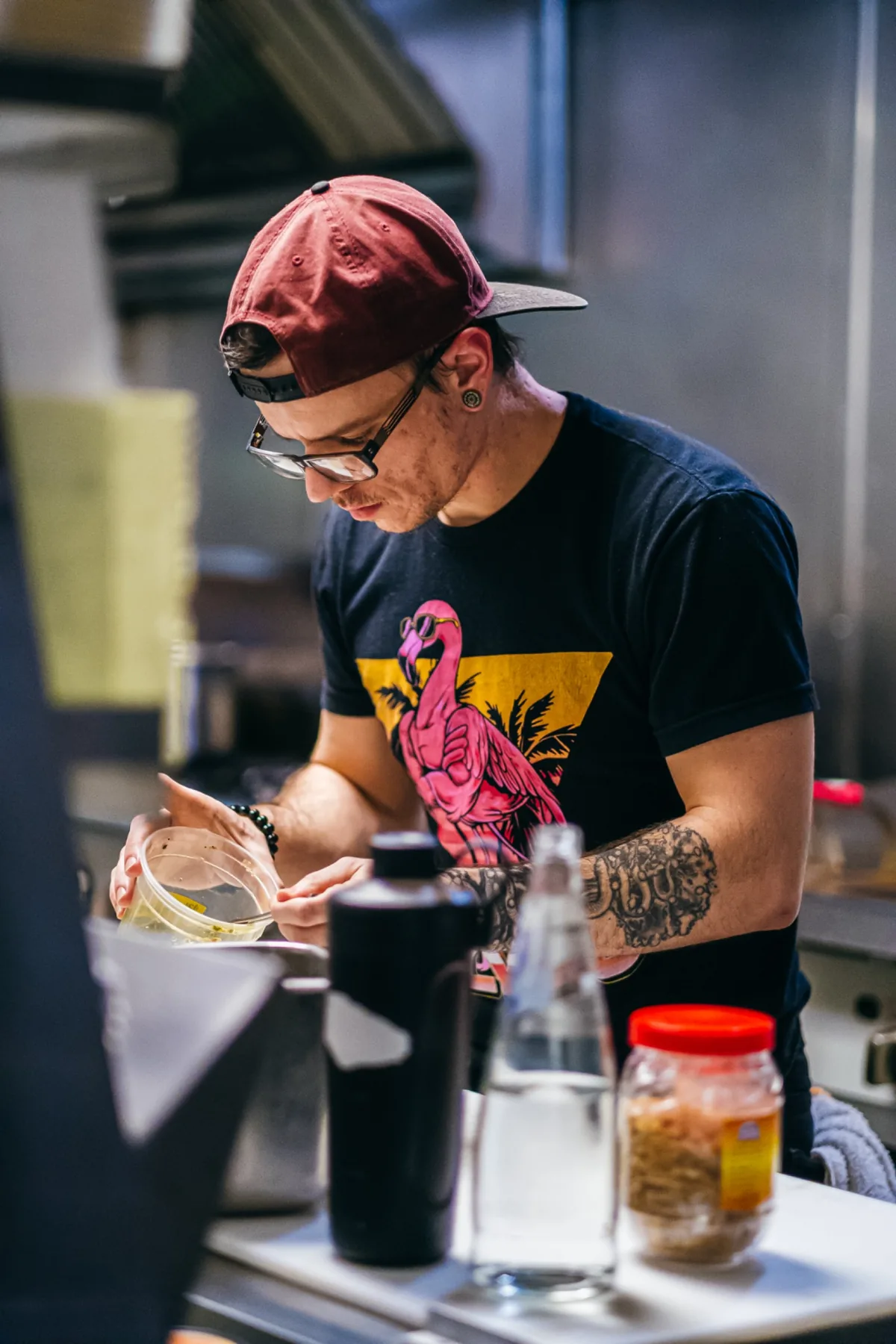 Cook in a graphic shirt mixing ingredients in a metal bowl.