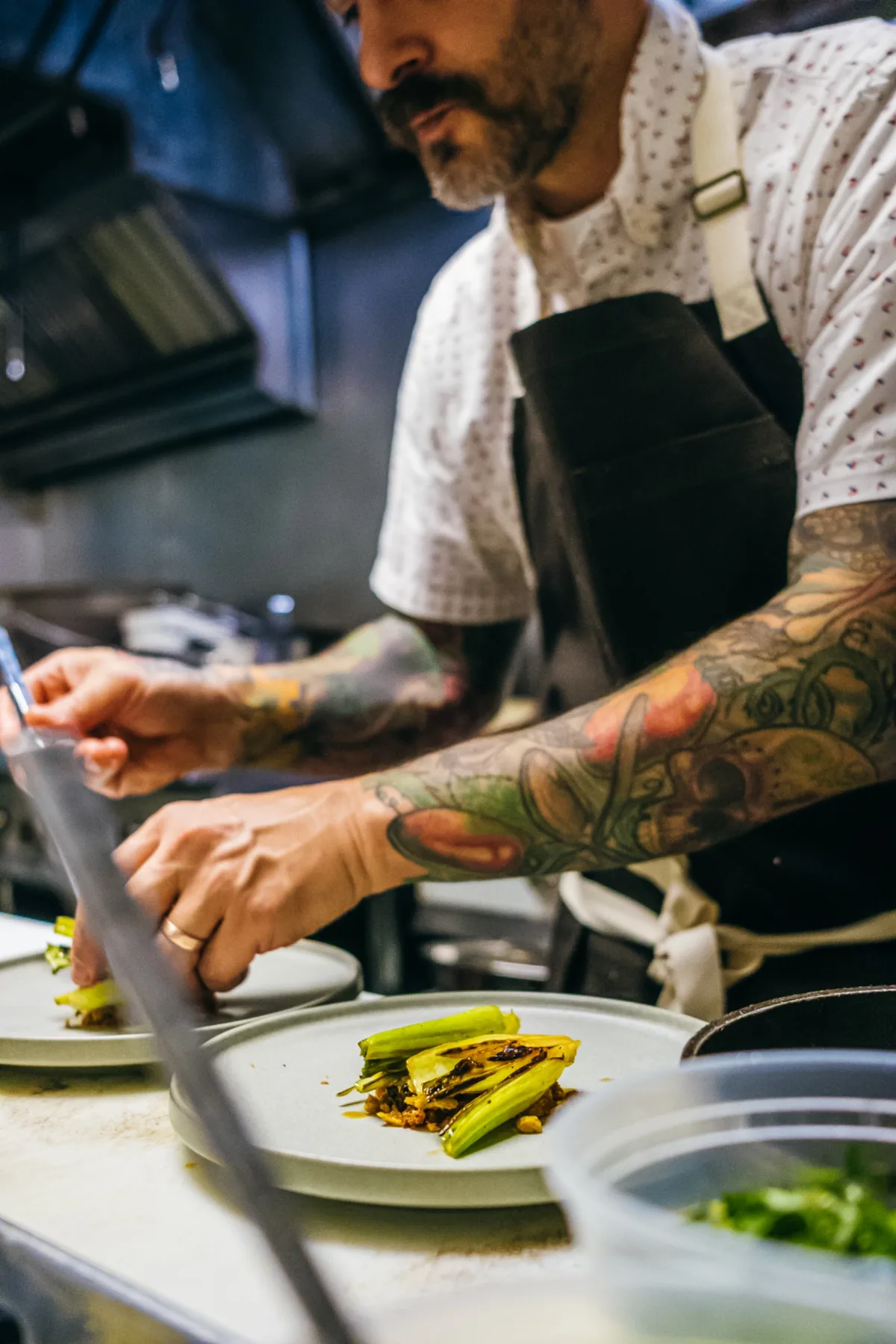 Tattooed chef preparing a dish at the kitchen counter.