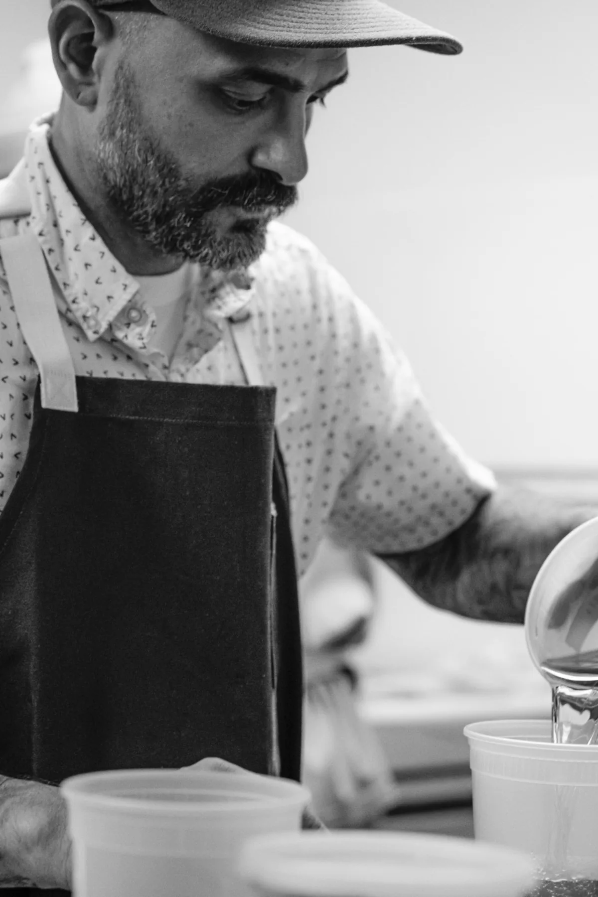 Chef in a dark apron working over a pan at the stove.