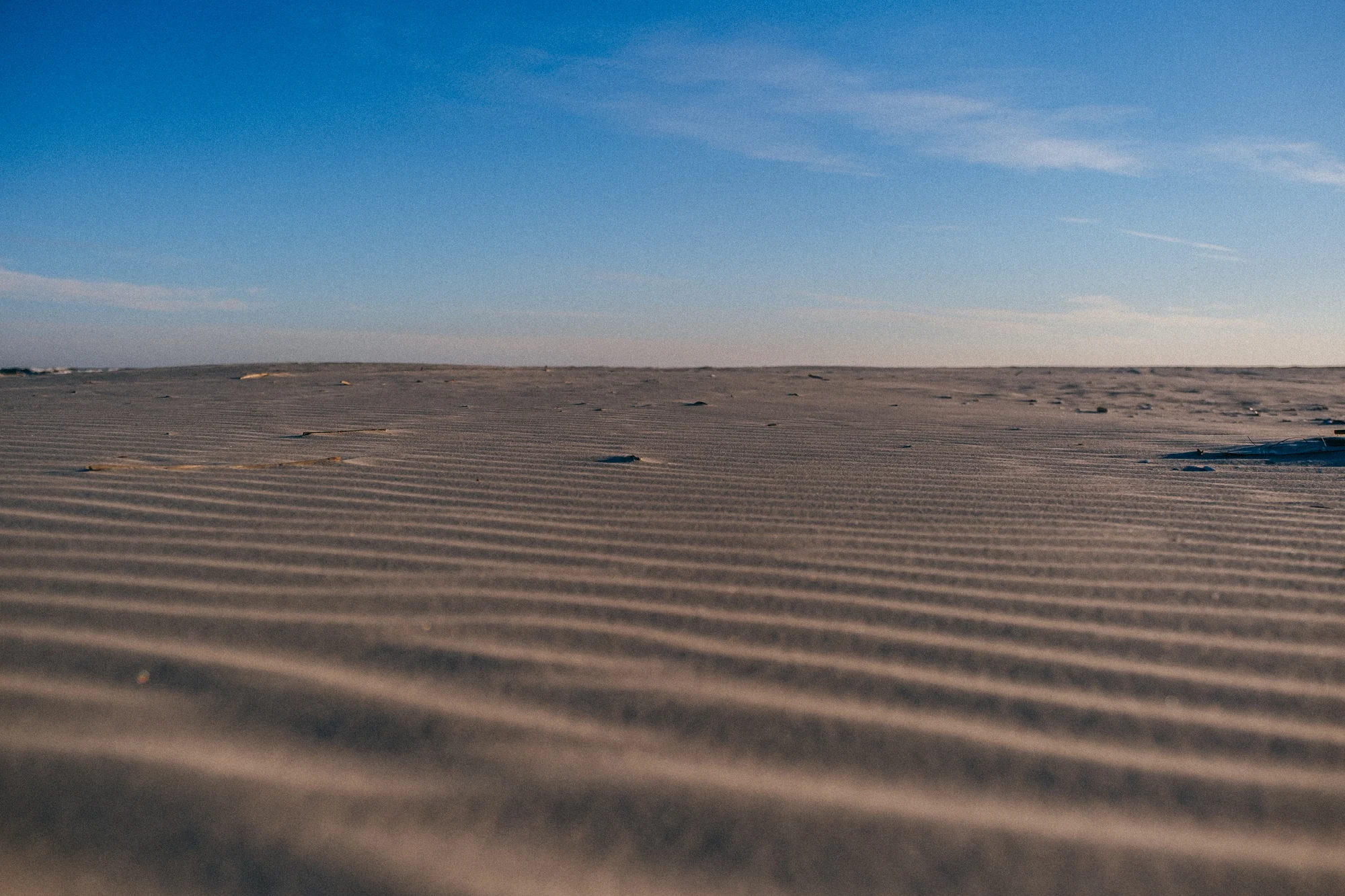 Low angle sandy beach with rippled sand leading to distant flat horizon under blue sky.