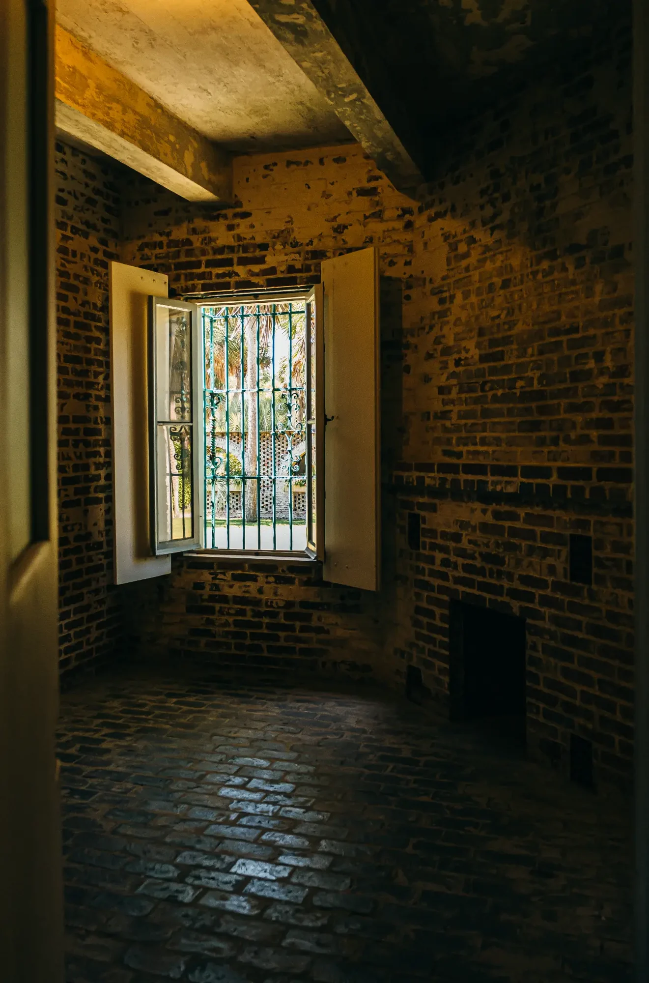 Sunlit barred window set in warm brick interior with textured cobblestone floor reflections.