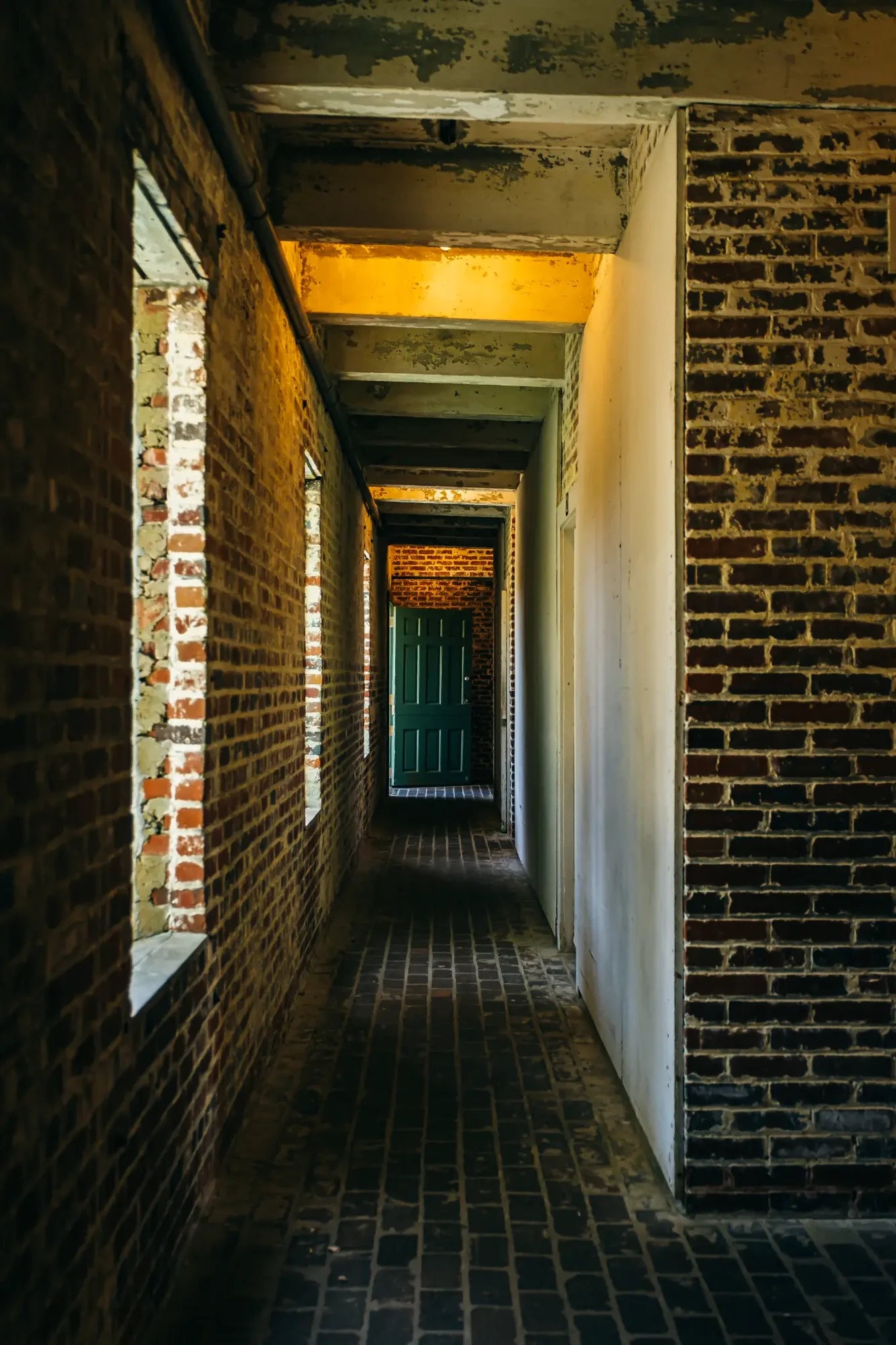 Narrow brick corridor with beams glowing warm yellow light and green door.