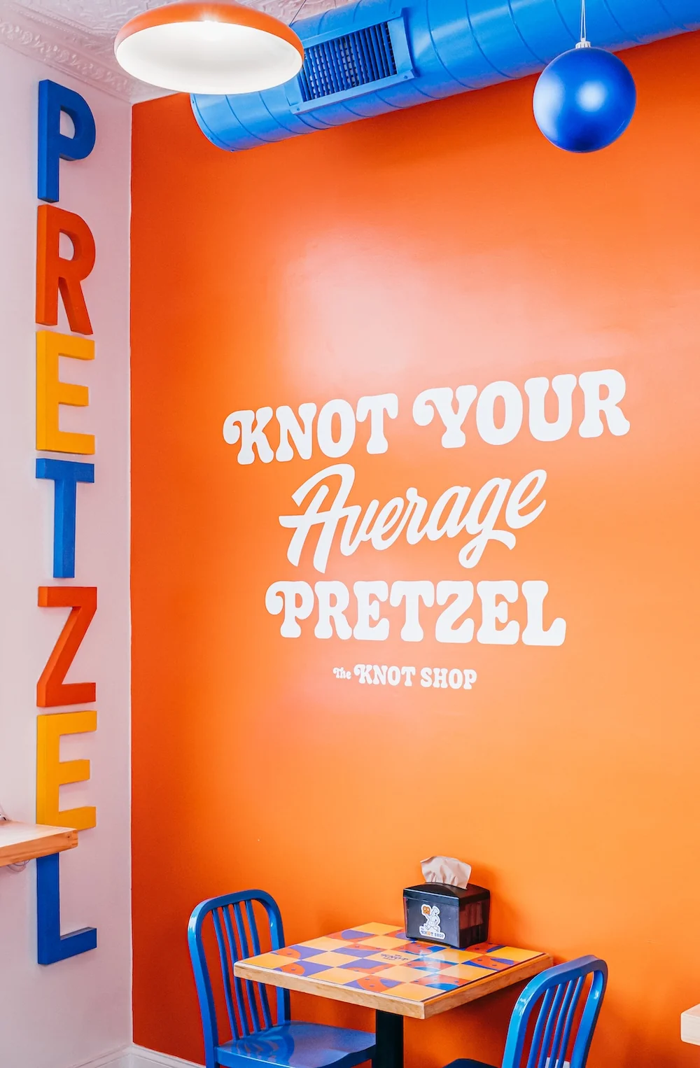 Bright orange interior wall with white slogan Knot Your Average Pretzel blue chairs.