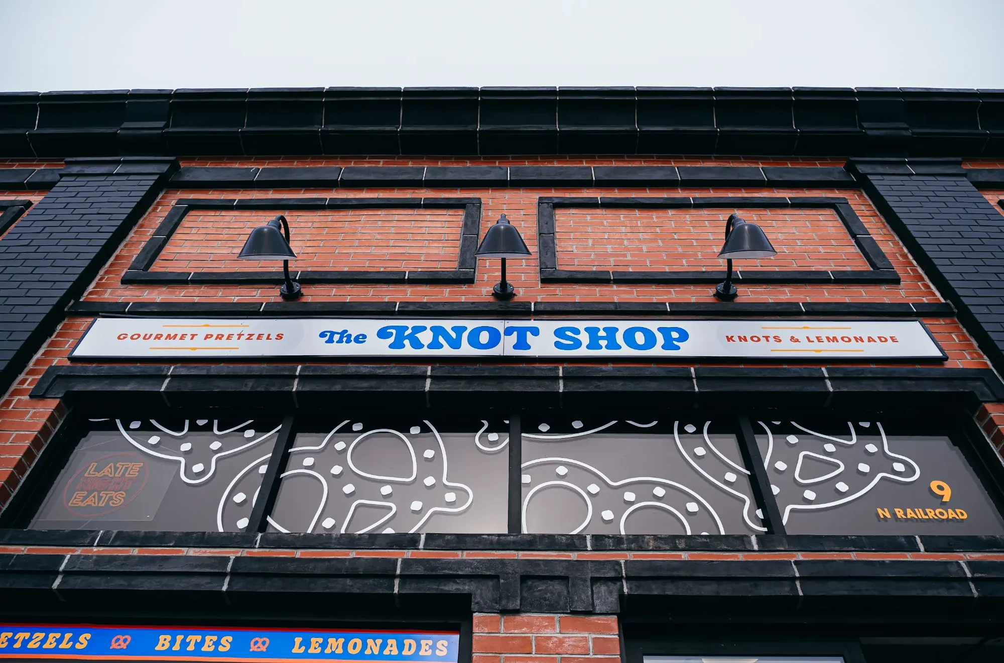 Low angle view of red brick storefront with three black lamps and blue sign.