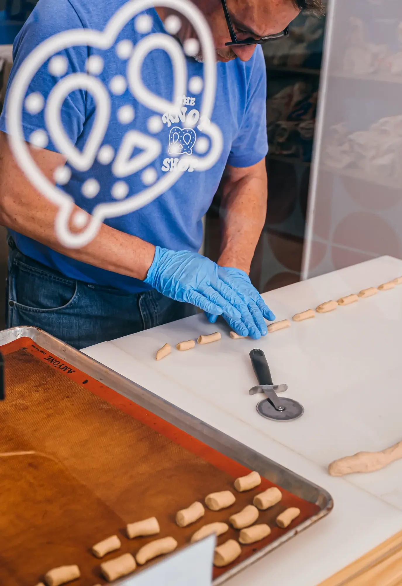 Hands in blue gloves arranging small dough pieces on white counter through decorative window decal.