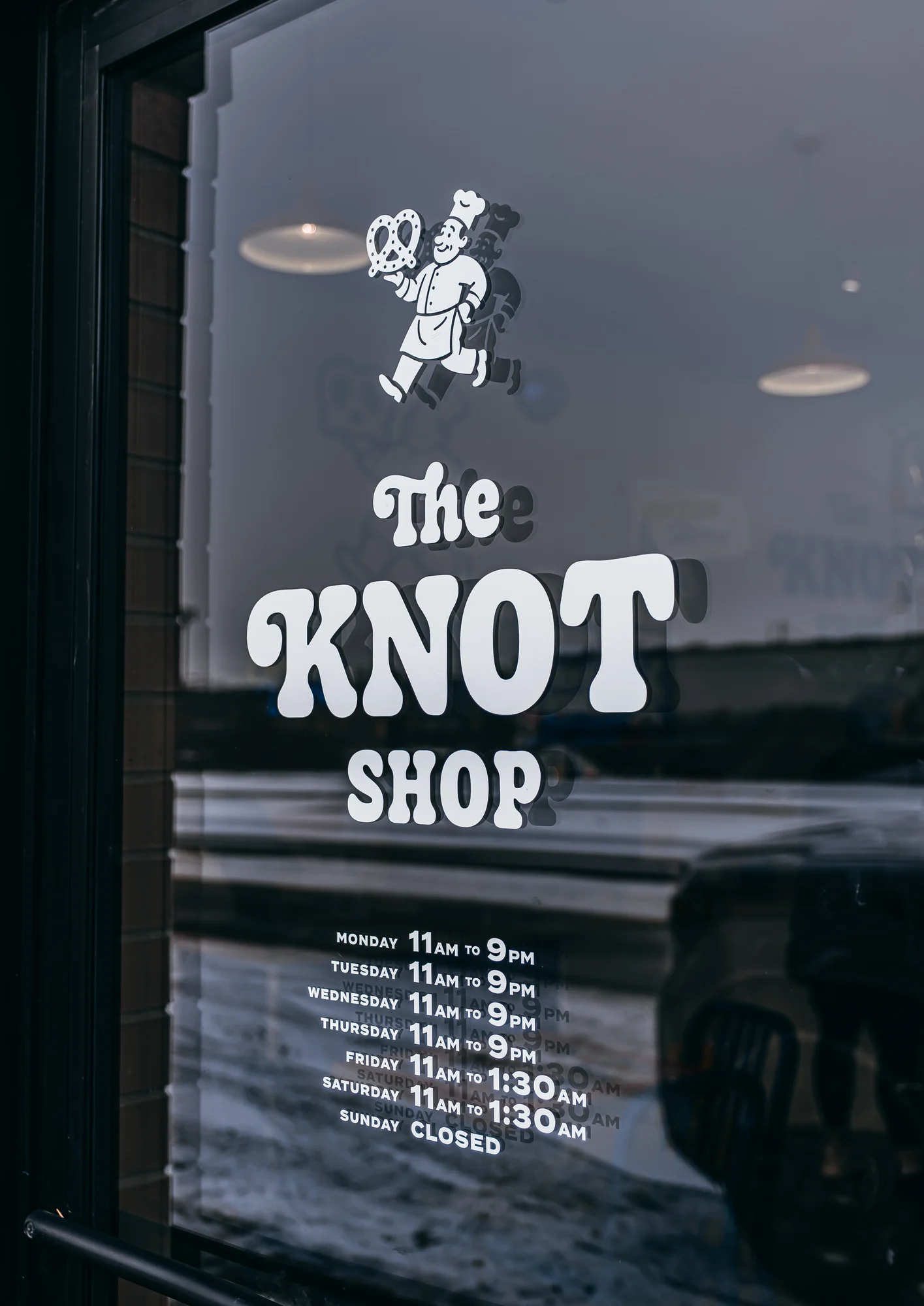 Glass door with white KNOT SHOP lettering and cartoon figure in chef hat holding pretzel.