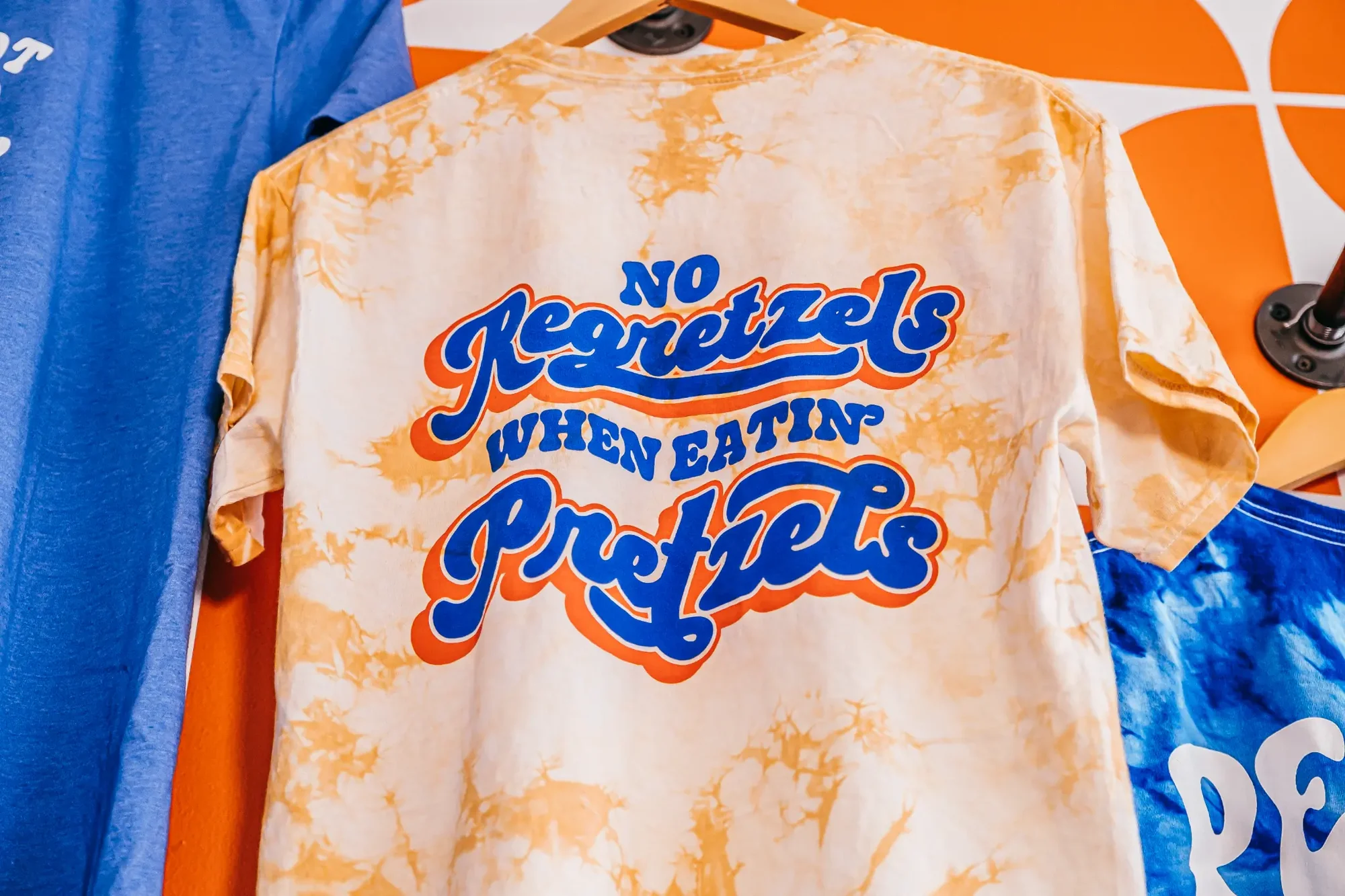 Hanging peach orange tie dye T shirt with bold blue and orange script graphic centered on back.