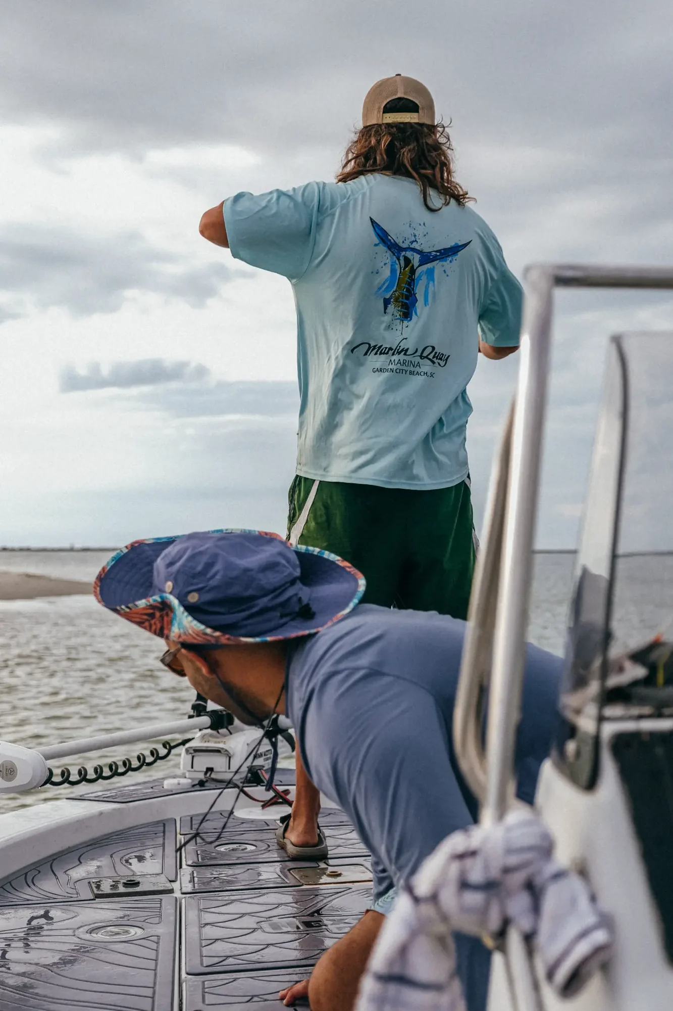 Two people on a boat deck with gear under overcast sky.