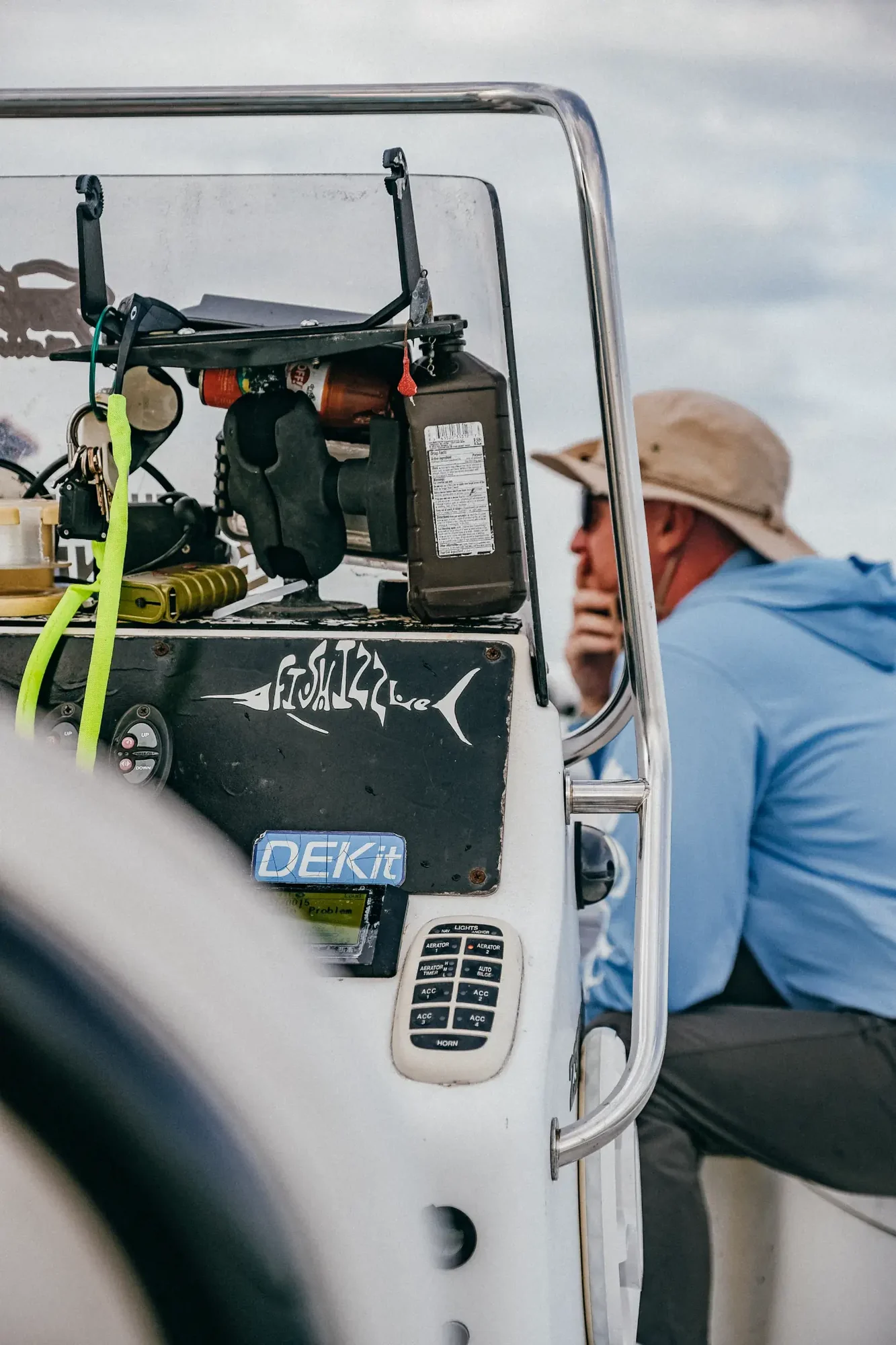 Close up boat console with neon green straps tools and controls and a blurred man in beige hat.