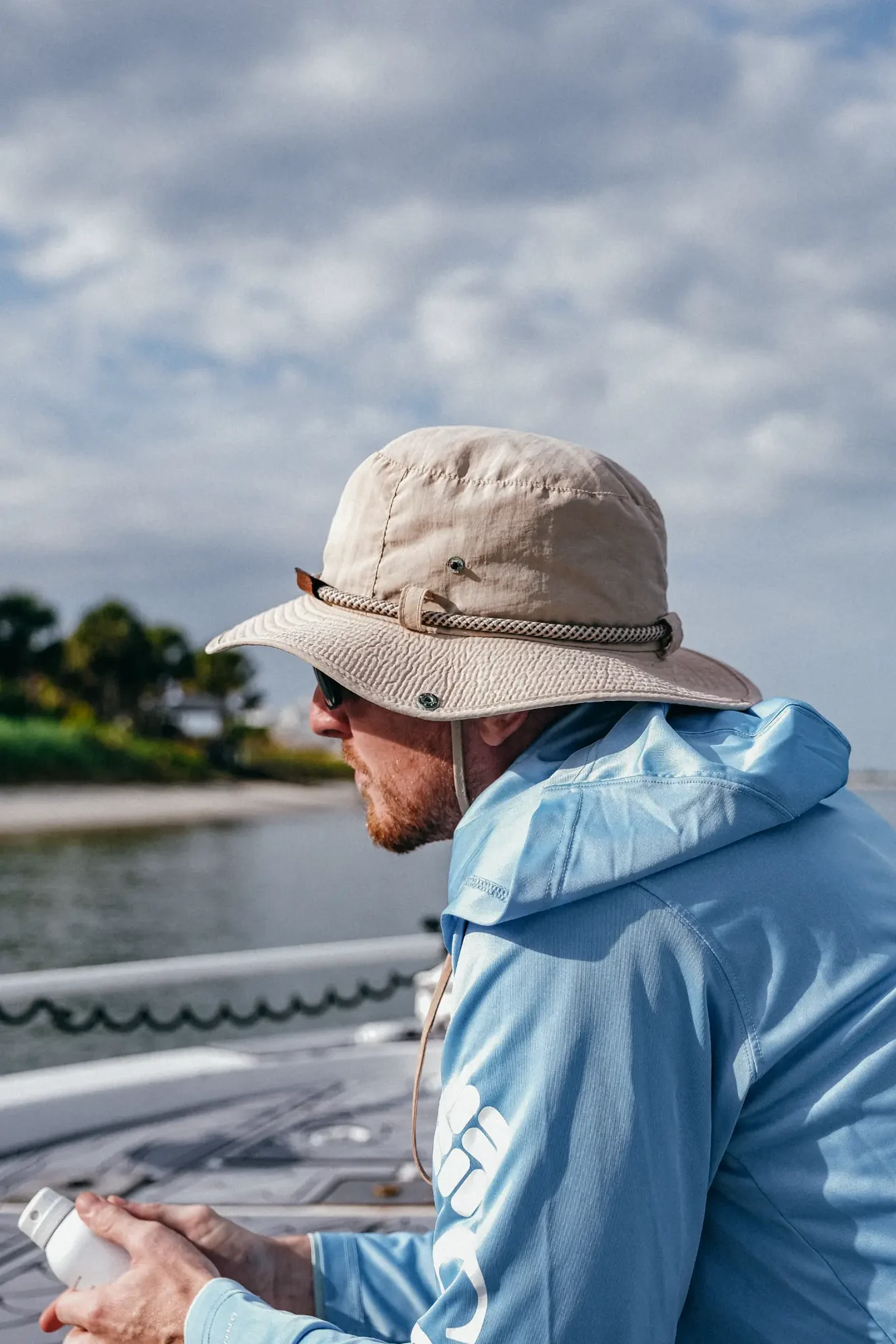 Side profile of a person wearing a beige hat and light blue jacket on boat.