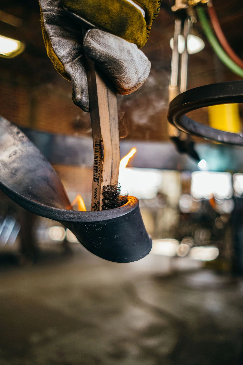Close view of gloved hands pouring molten metal into a dark crucible in the workshop.