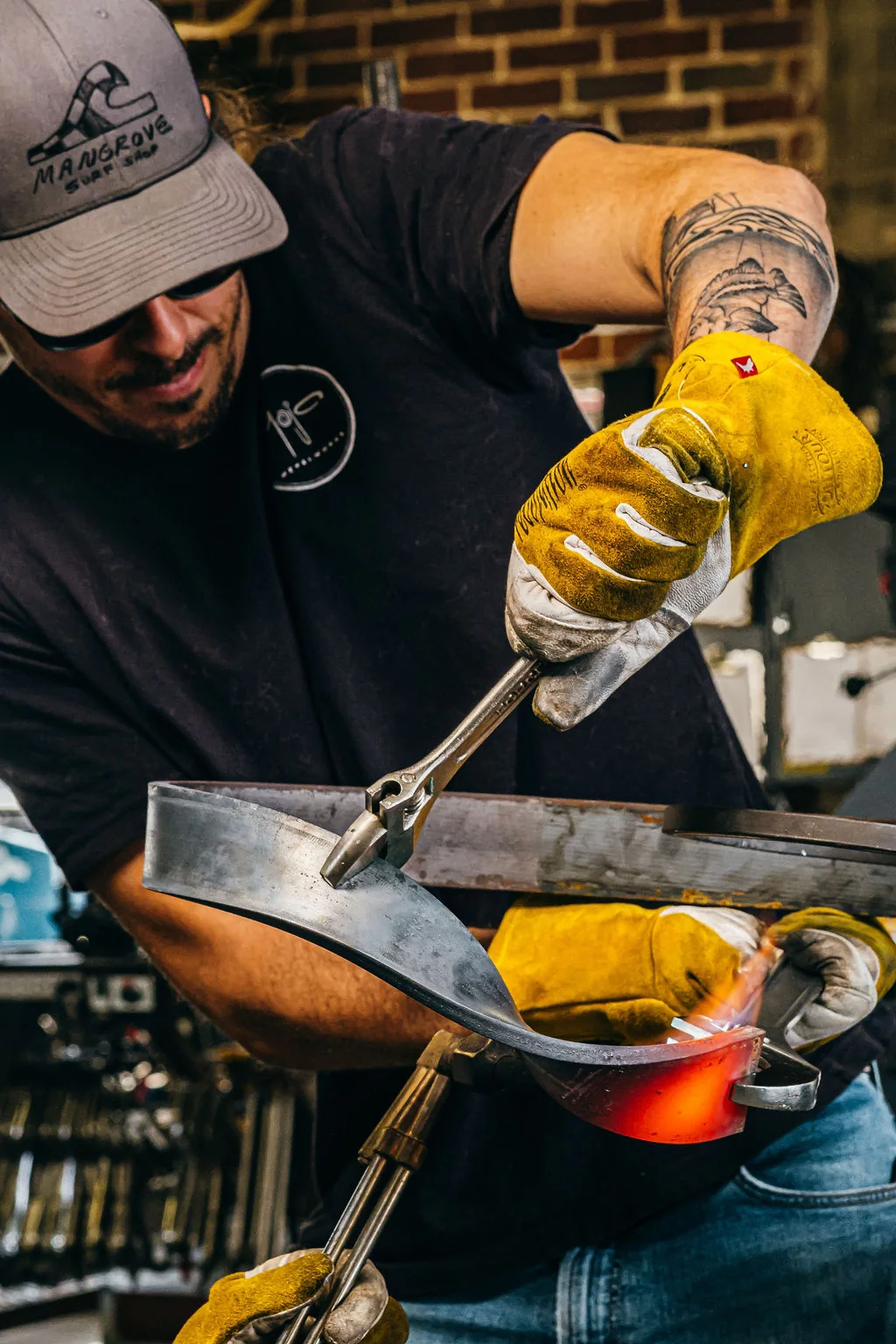 Metalworker in yellow gloves shaping a heated steel form in the workshop.