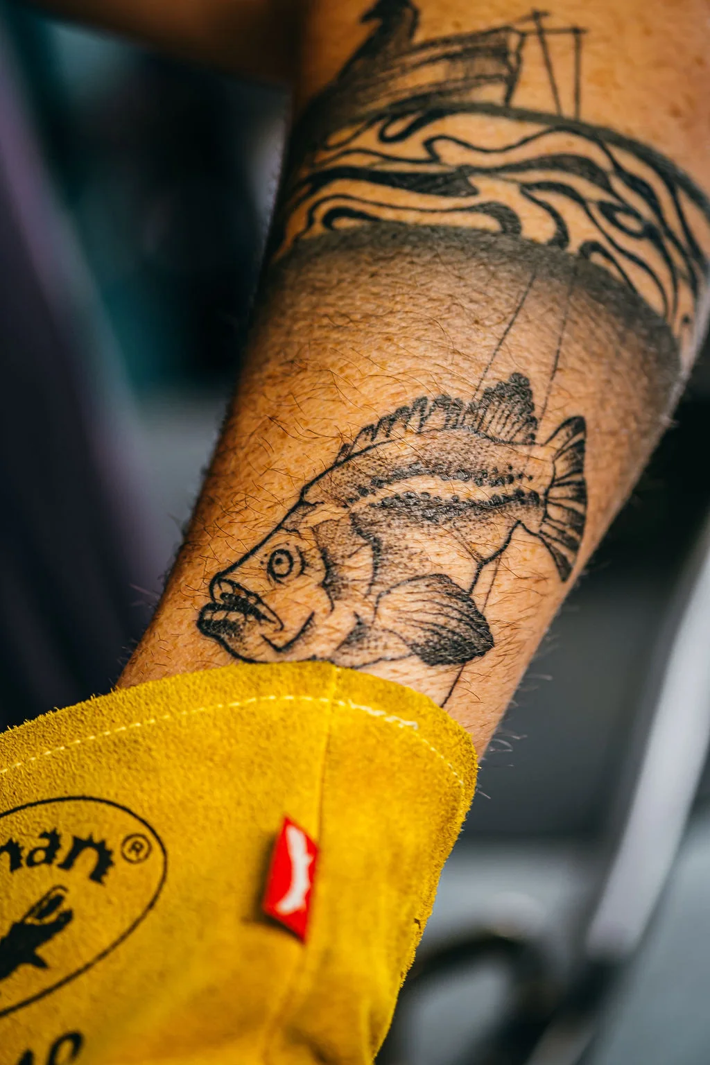 Detail of a tattooed forearm and yellow work glove at Mojo Metal Works.