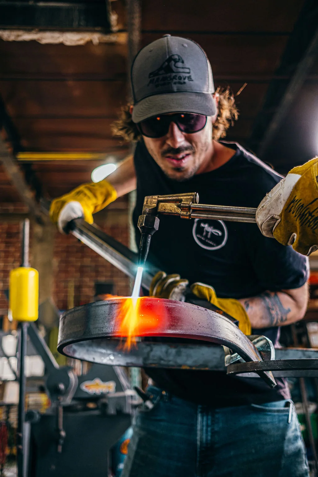 Metalworker holding a torch over a glowing steel vessel inside the studio.