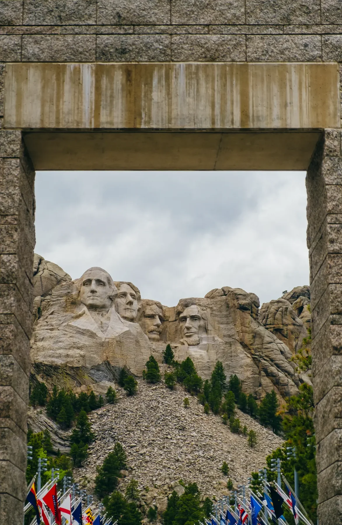 Mount Rushmore framed through a granite arch with state flags below.