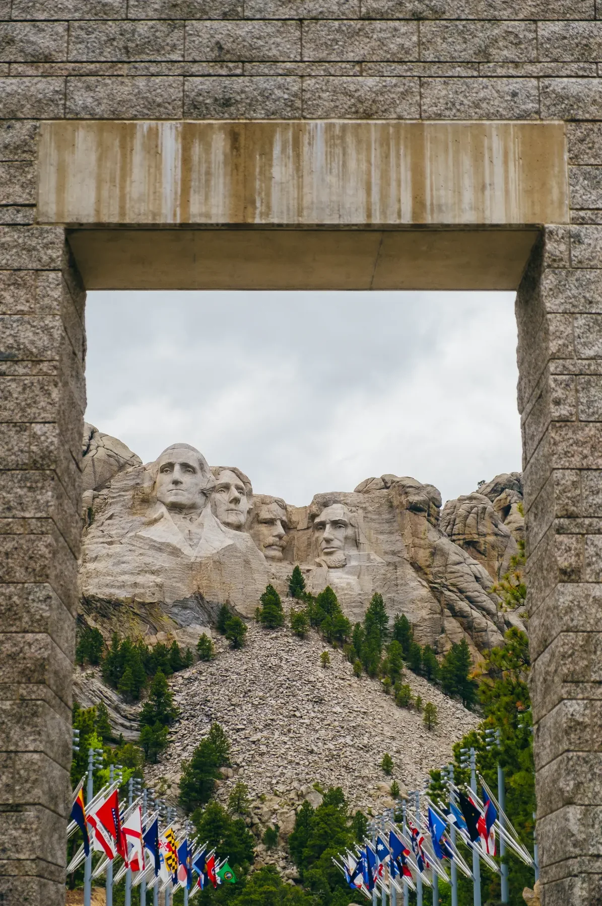 Mount Rushmore seen through a granite arch and rows of state flags.