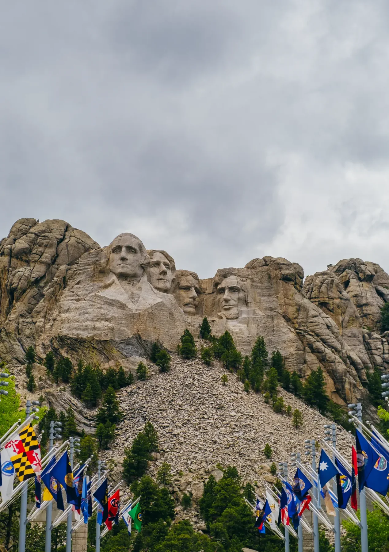 Mount Rushmore above a forested slope and state flags.
